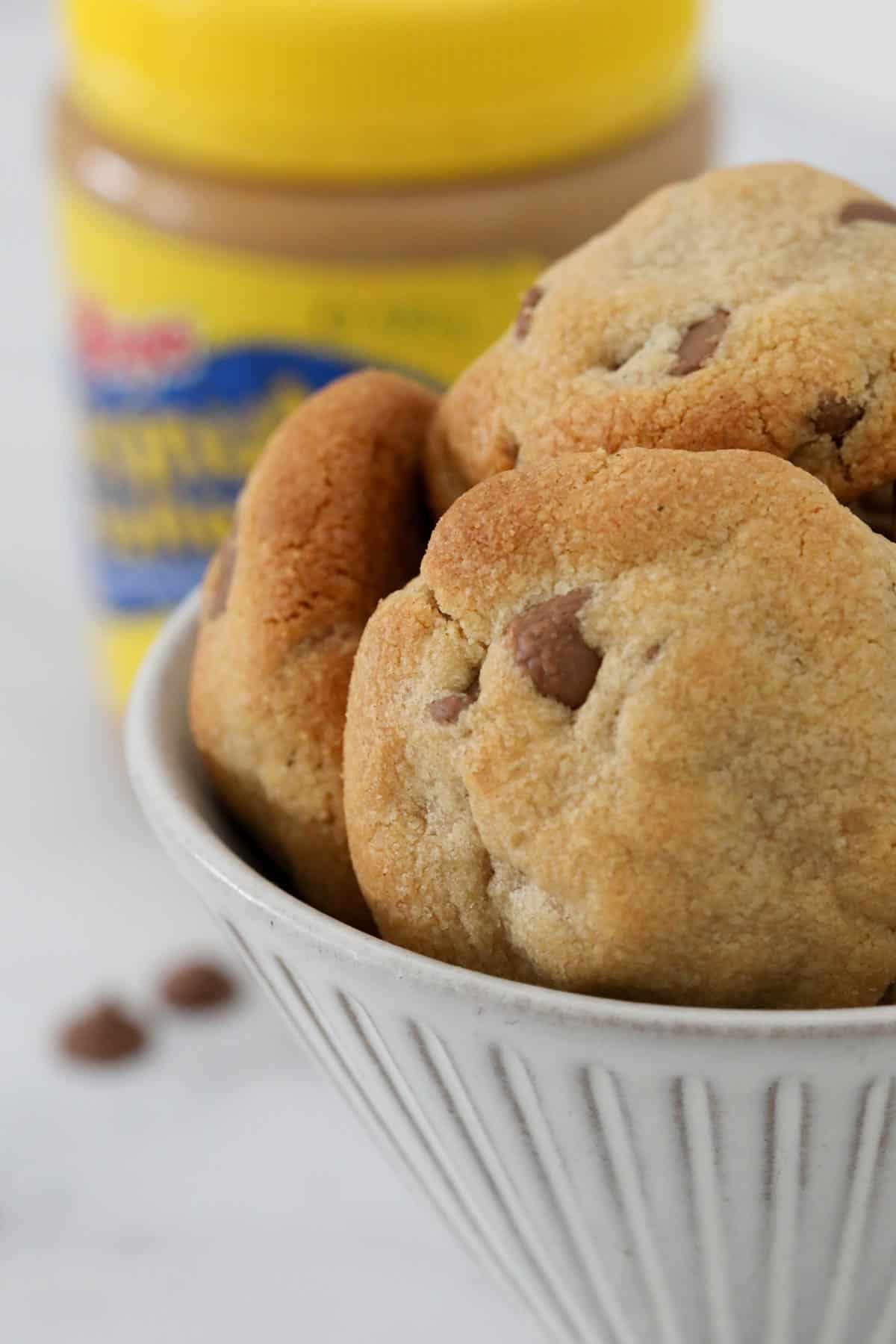 Chocolate chip peanut butter cookies in a bowl, with a jar of peanut butter just visible behind.
