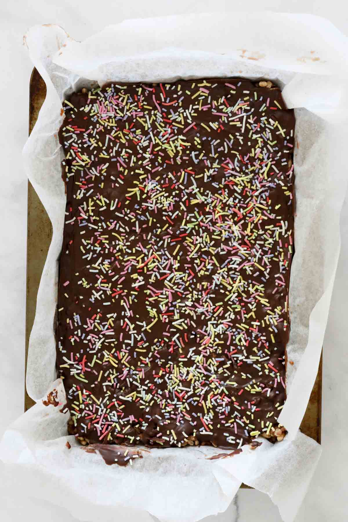 The slice in the tin topped with melted chocolate and sprinkles.