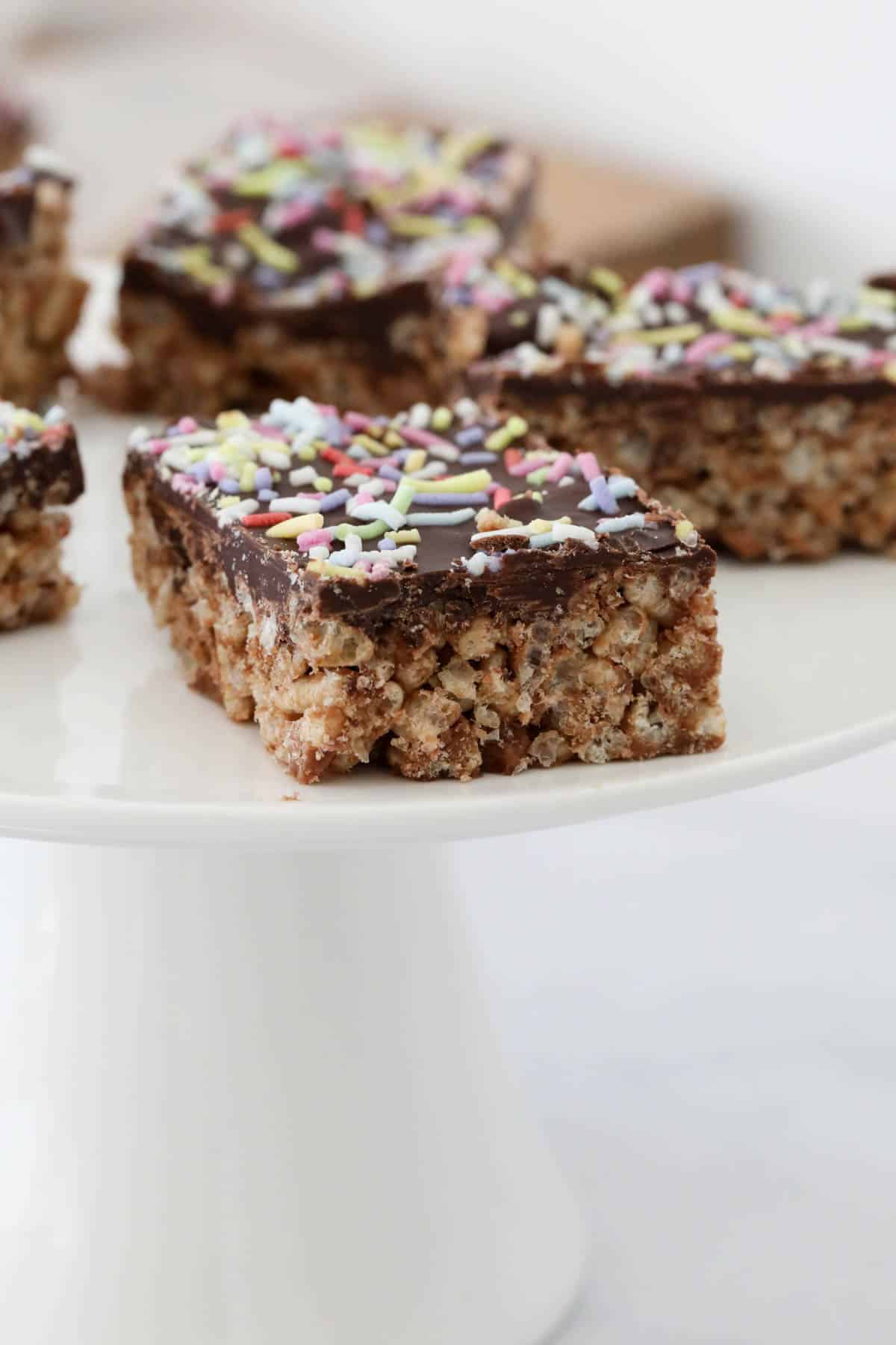 Bars of chocolate Rice Bubble slice on a white cake stand.