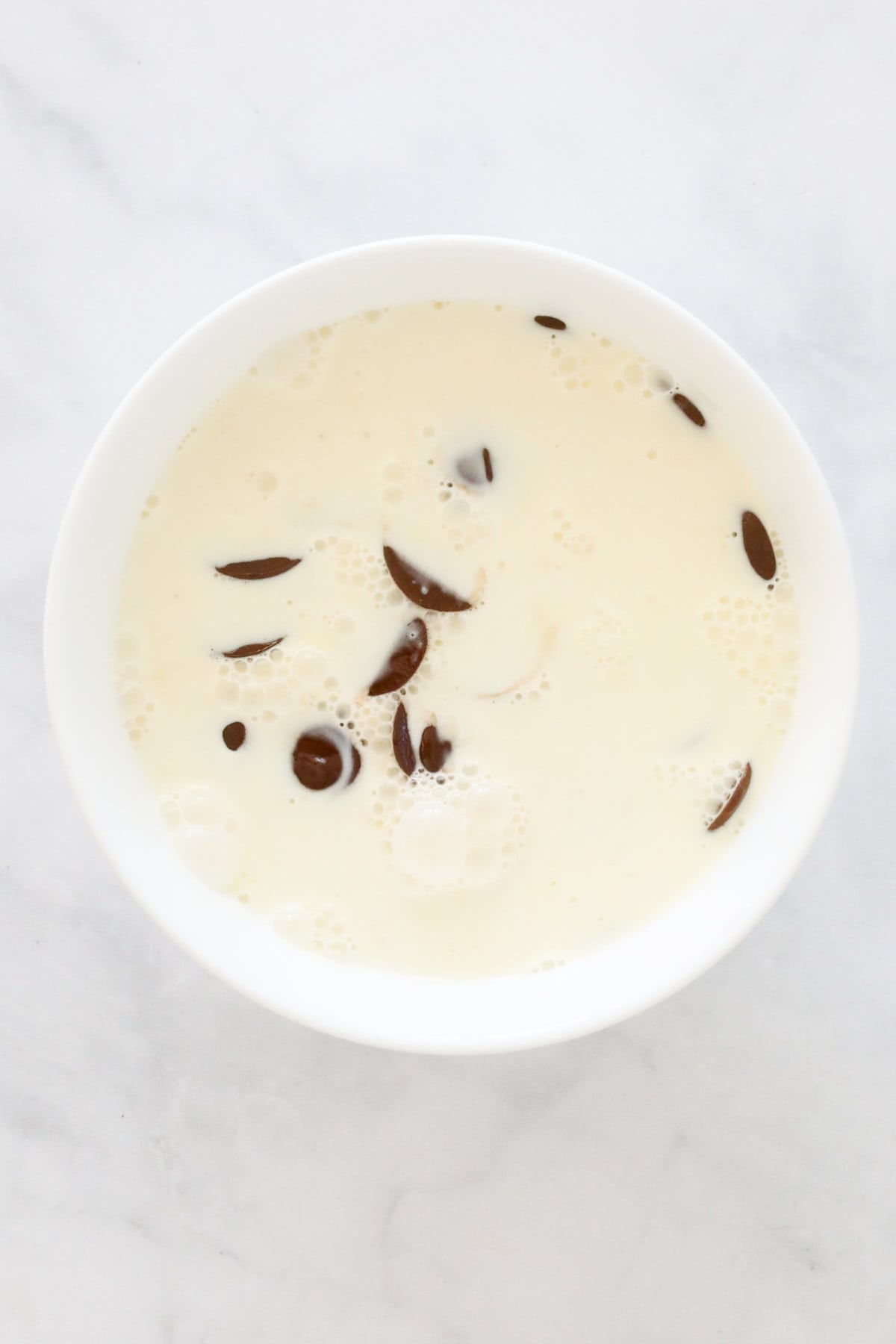 Hot cream poured over the chocolate melts in a bowl.