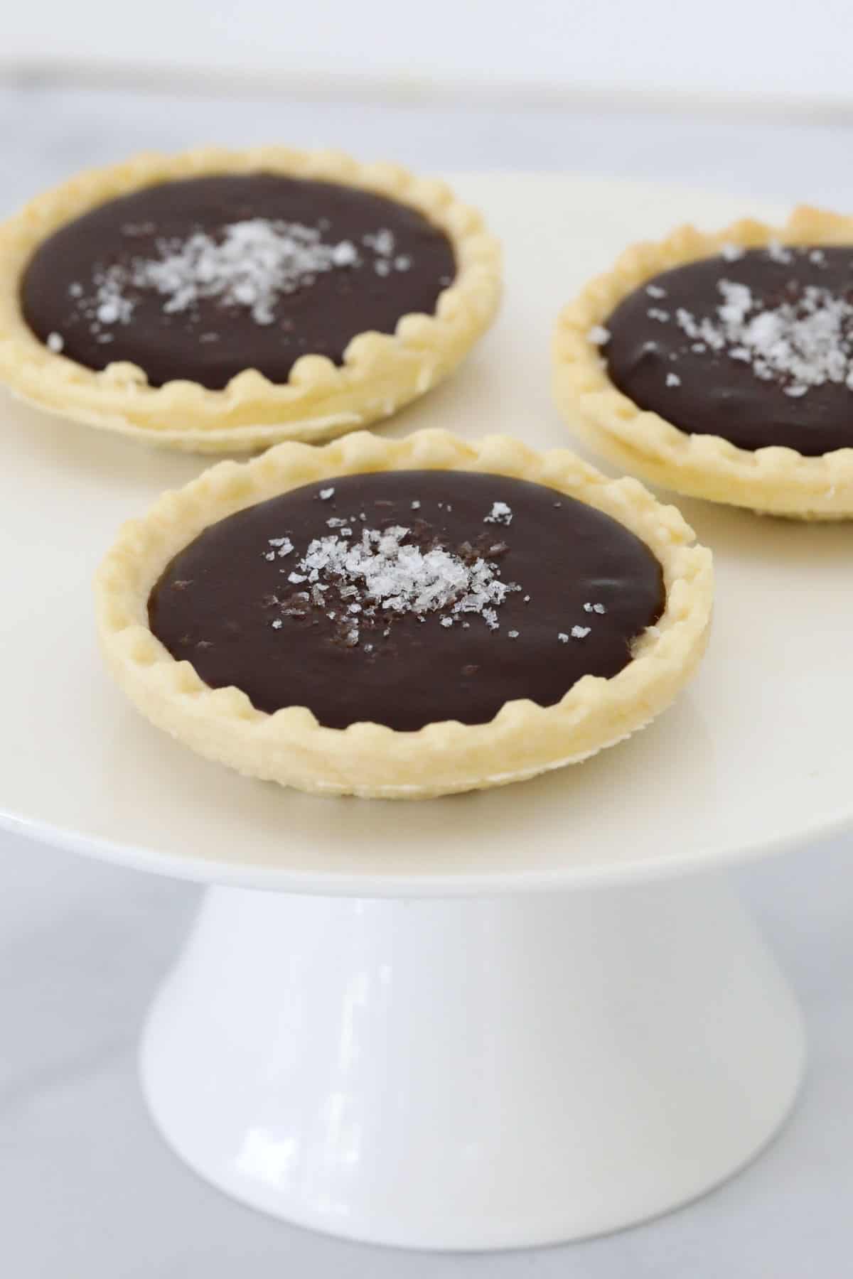 Mini chocolate tarts on a white cake stand.