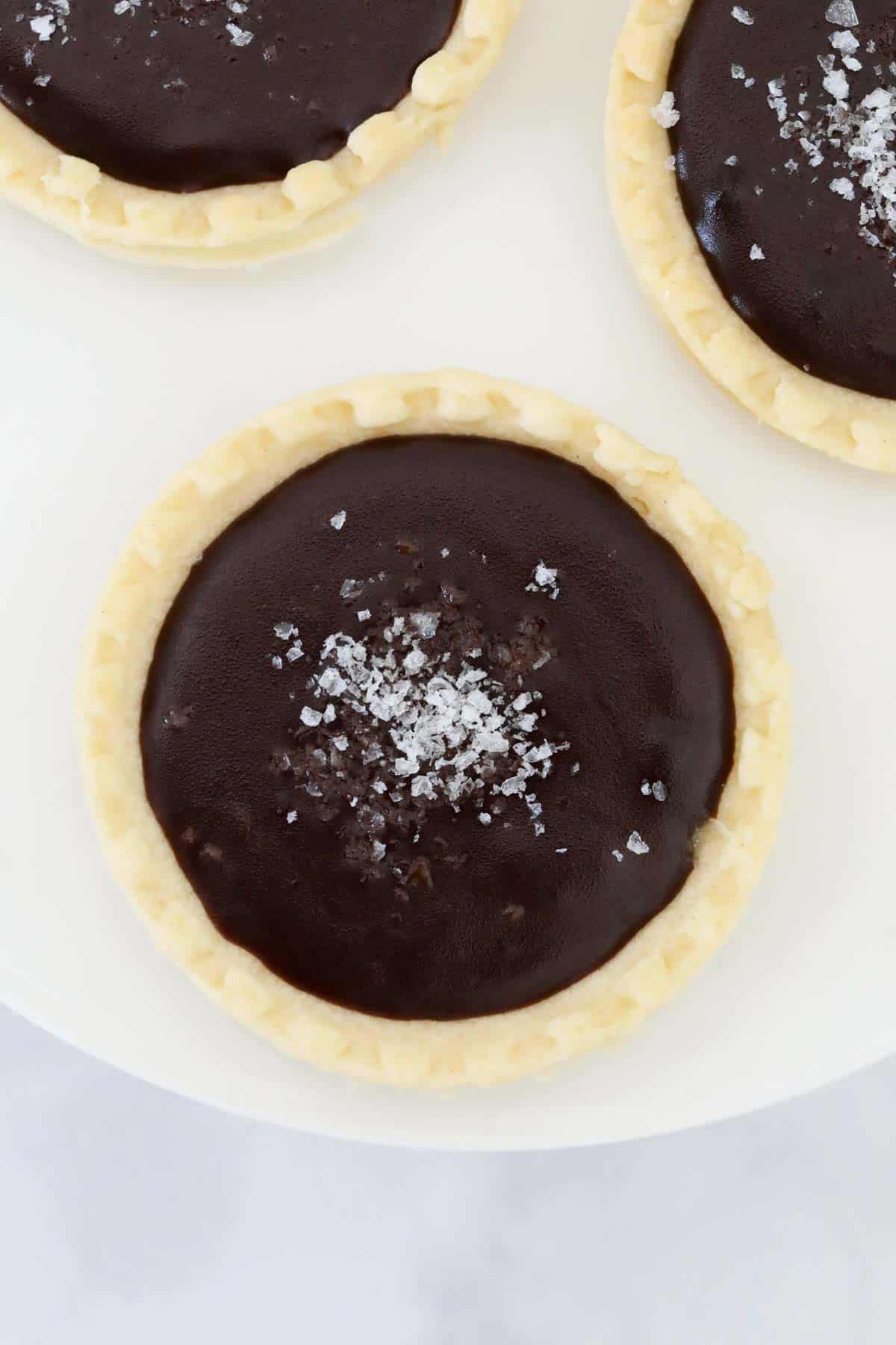 Overhead photo of the mini chocolate tarts, sprinkled with sea salt, on a white cake stand.