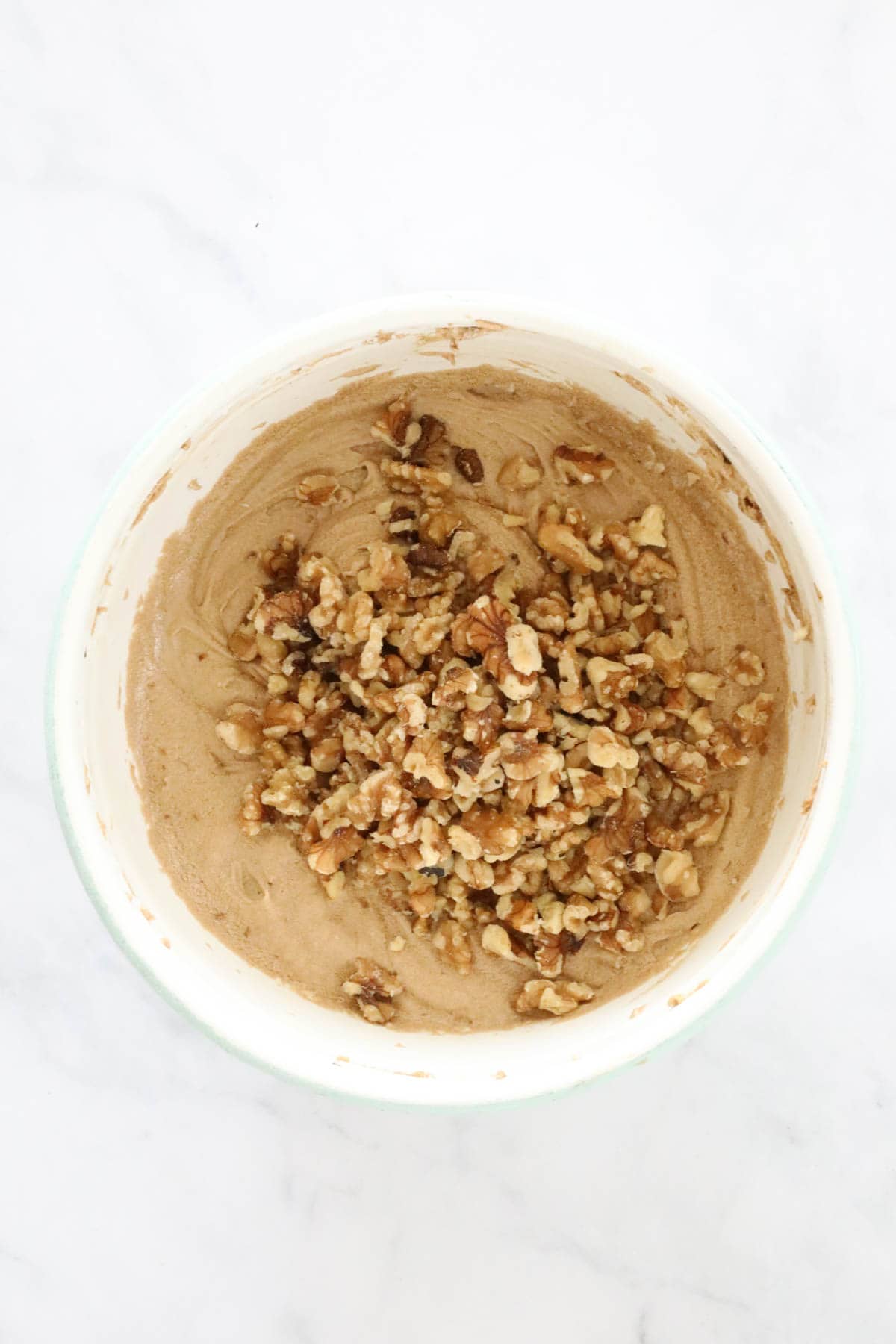 Chopped walnuts added to the loaf mixture in a white mixing bowl.