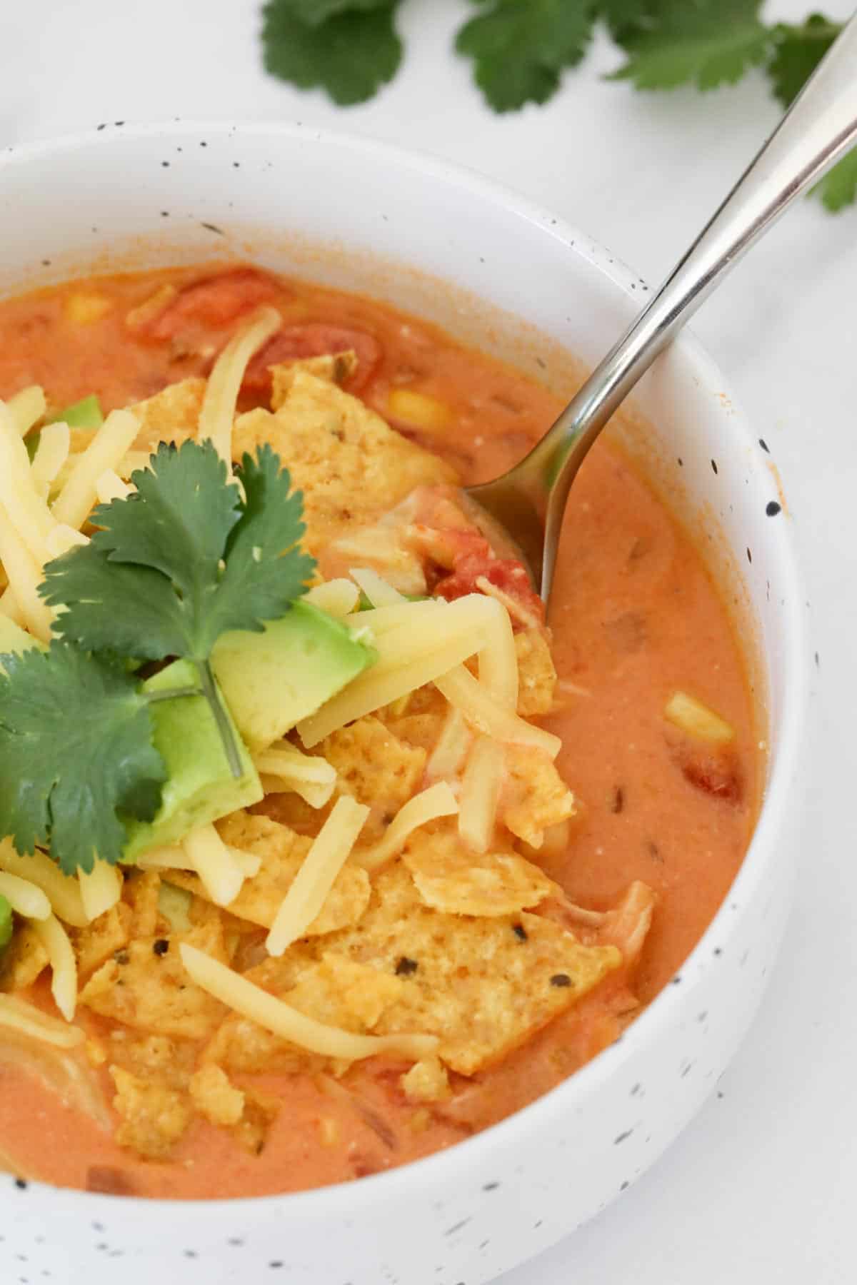 A bowl of chicken taco soup topped with corn chips, cheese and avocado.