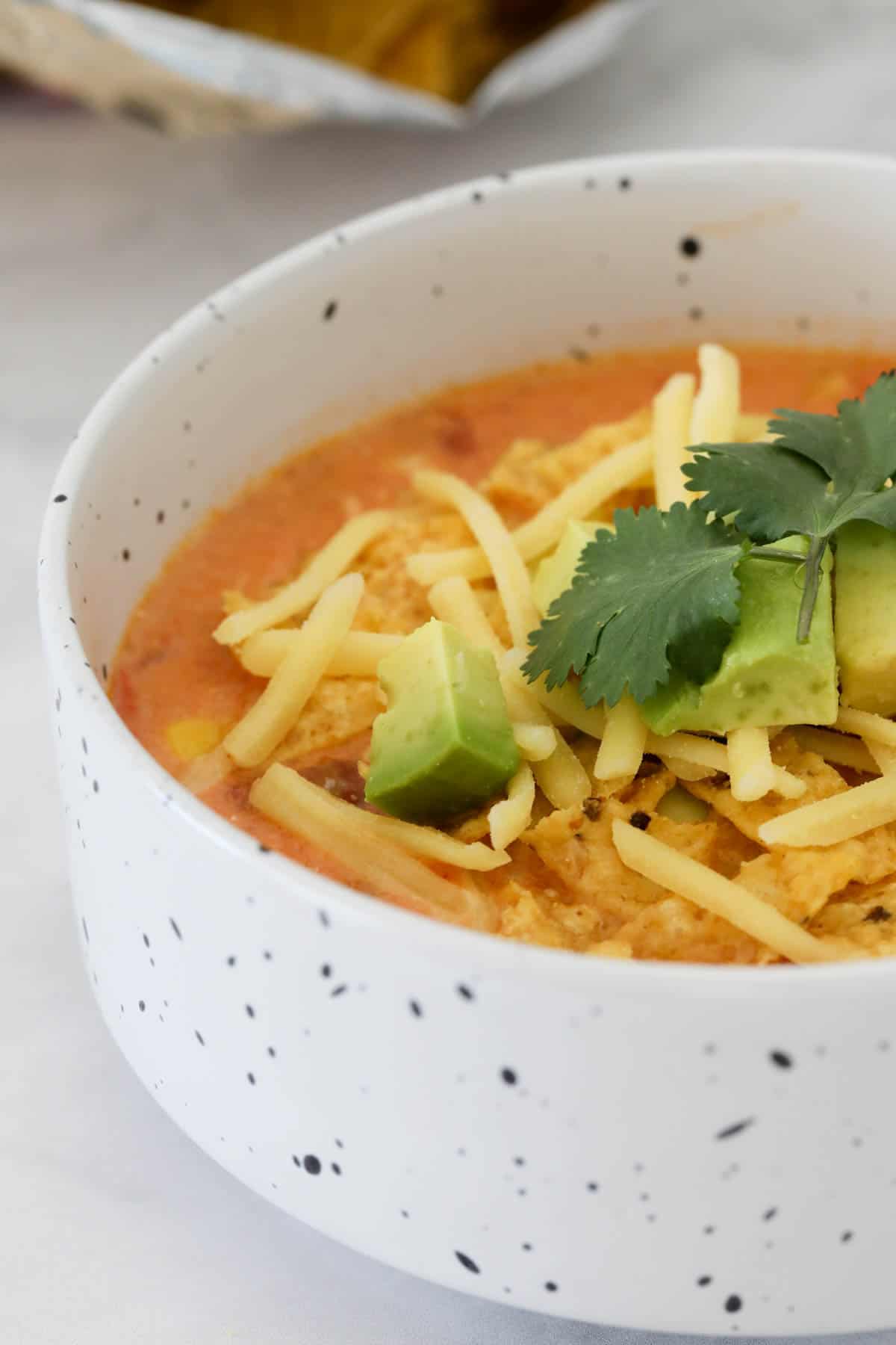 Side view of a bowl of chicken taco soup topped with grated cheese and avocado.