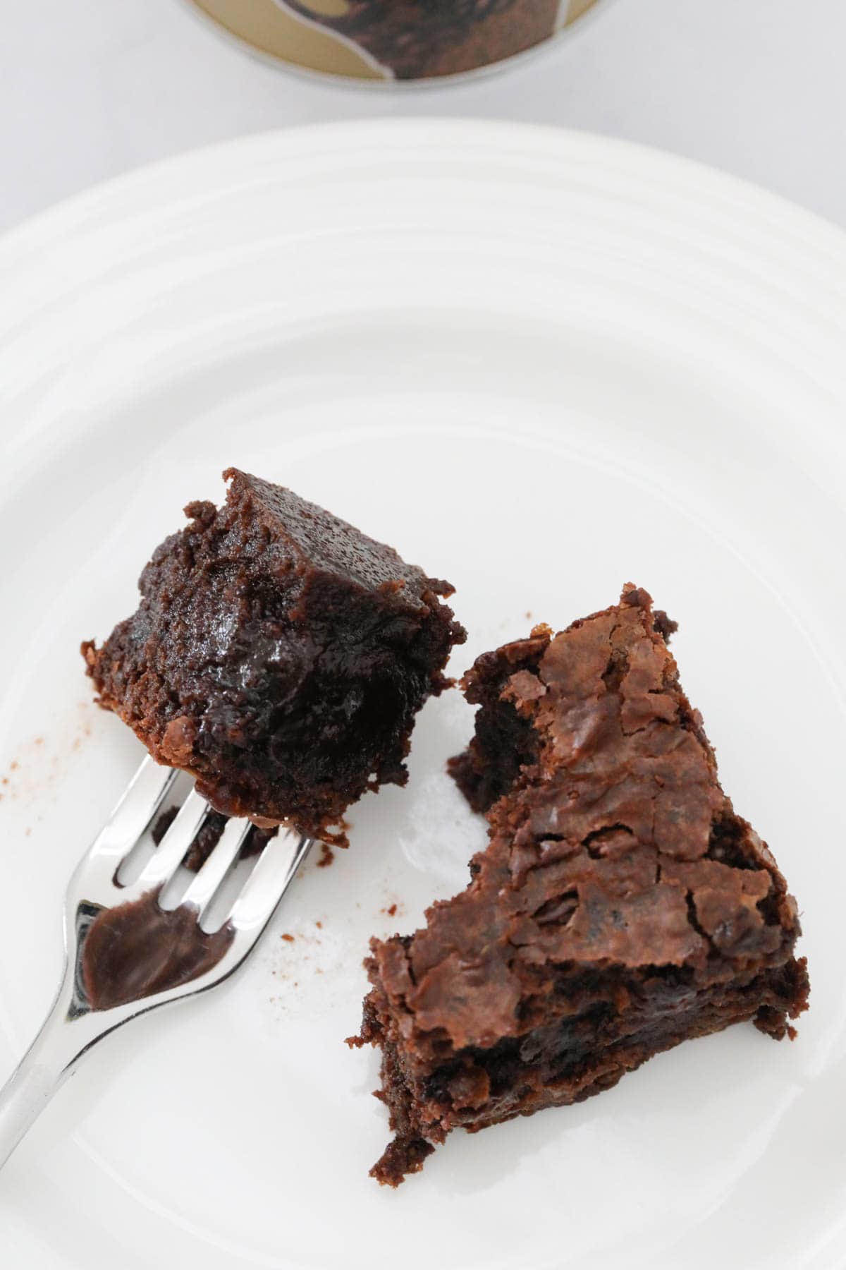 A square of brownie on a plate, with some on a fork beside.