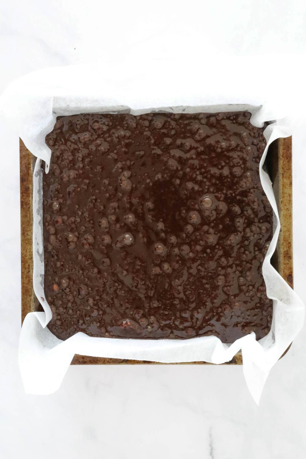 Brownie batter poured into a square baking tin lined with baking paper.