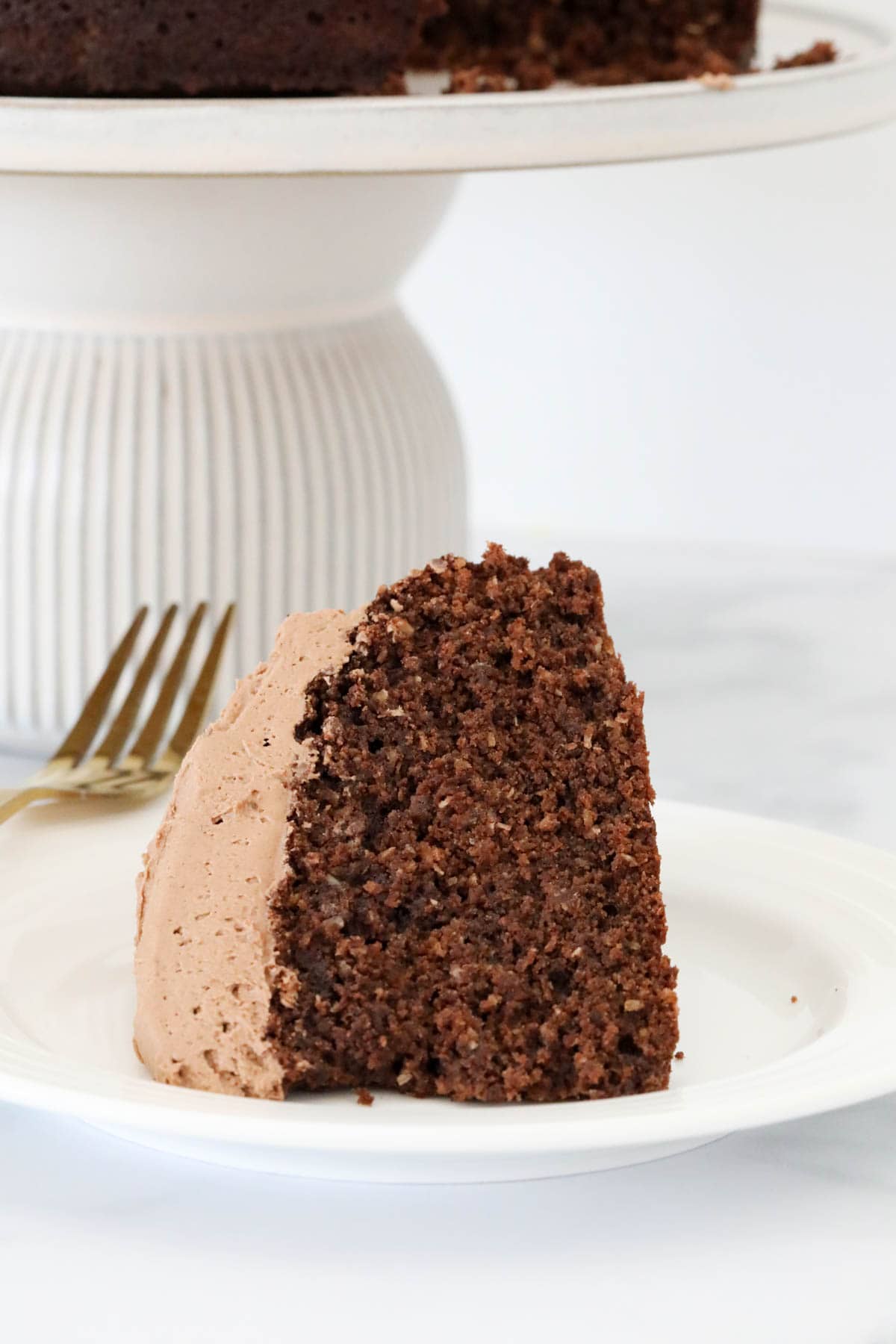 A wedge of chocolate cake with buttercream icing on a serving plate.