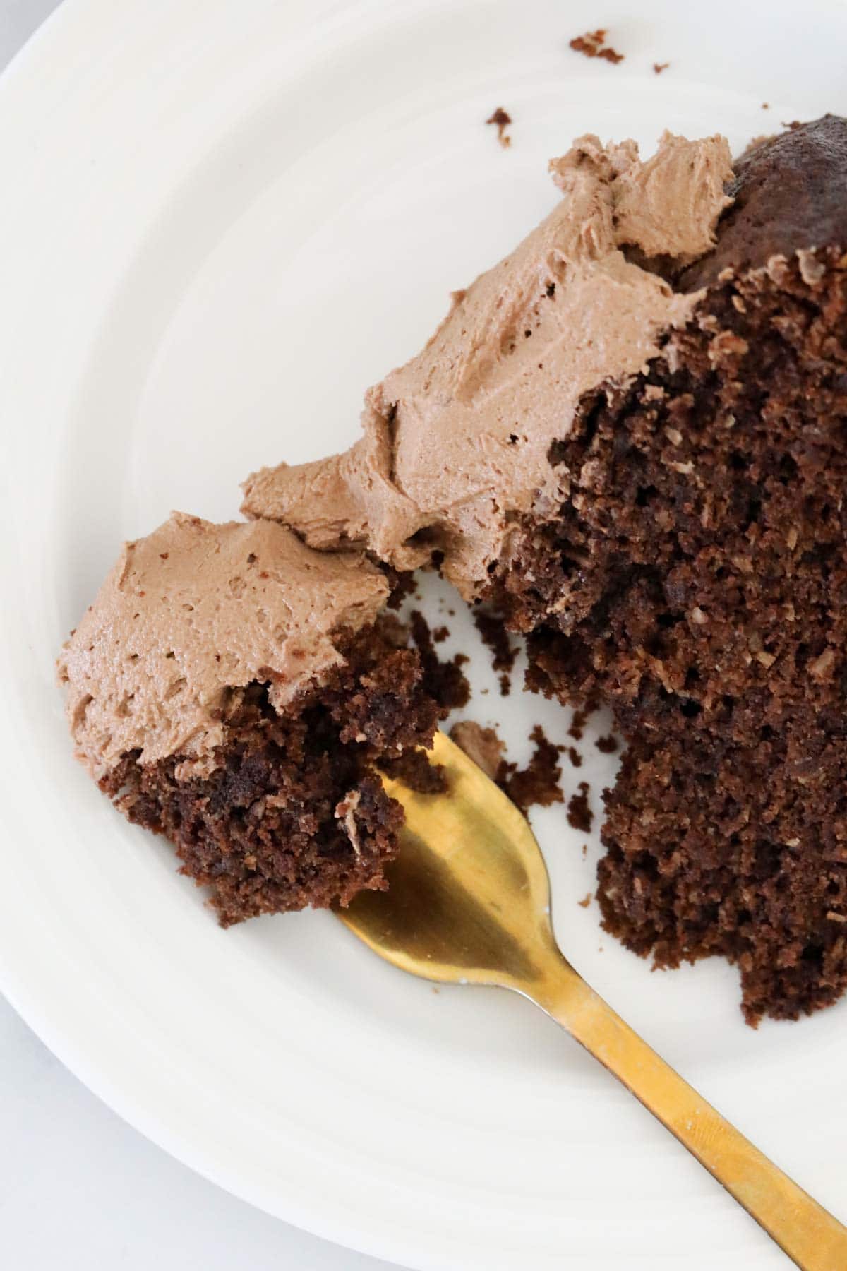 A forkful of chocolate cake with chocolate buttercream on a white plate.