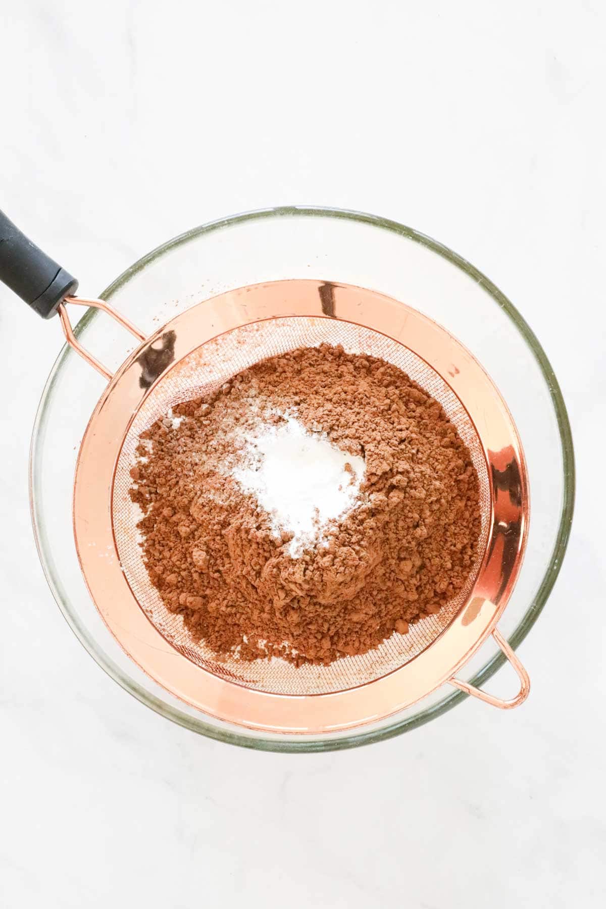 Flour, cocoa powder and baking powder in a sieve over the bowl of butter and eggs.