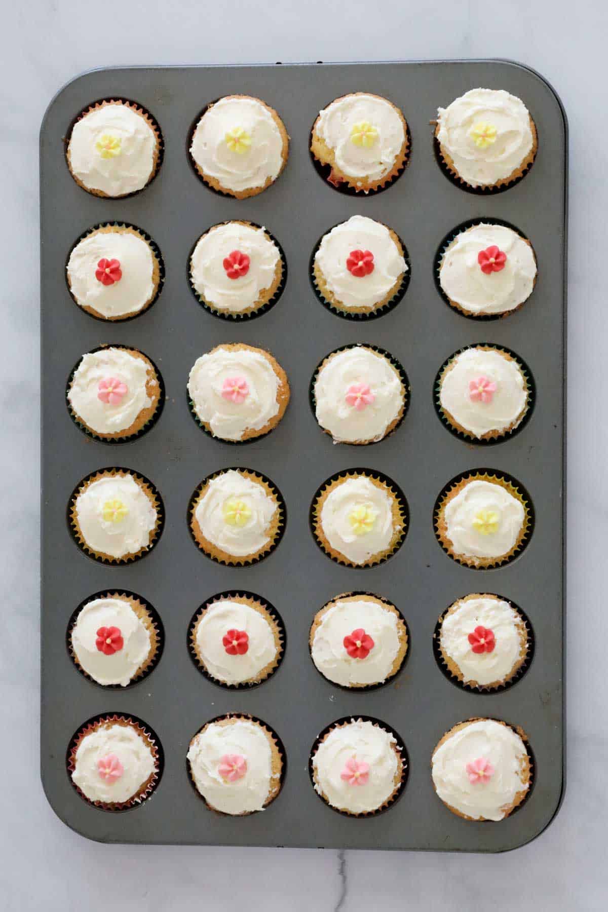 Frosted and decorated mini cupcakes in a baking tray.