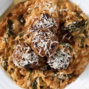 An overhead show of a bowl of creamy tomato risoni with baked pork meatballs on top and sprinkled with parmesan.