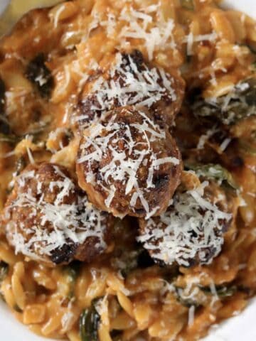 An overhead show of a bowl of creamy tomato risoni with baked pork meatballs on top and sprinkled with parmesan.