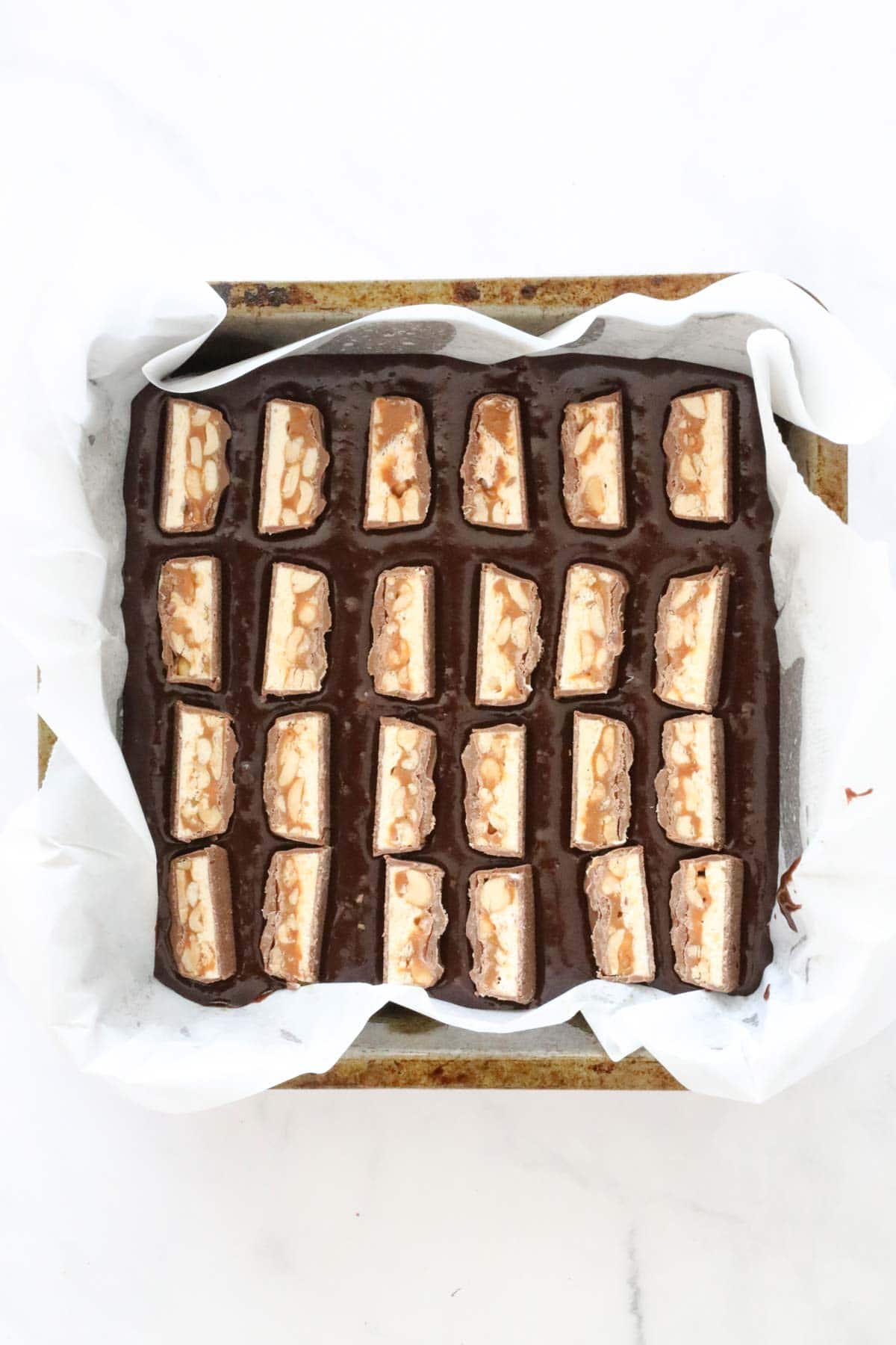 Slices of Snickers bars placed on the brownie batter in the tin.