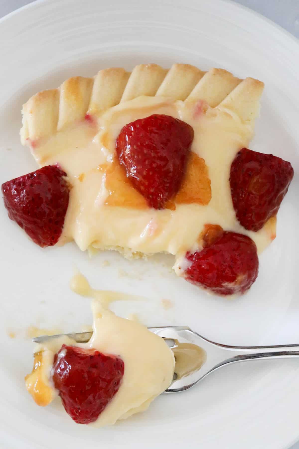 An overhead shot of a slice of strawberry flan on a white plate, with some on a fork beside.