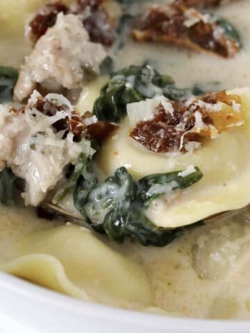 A bowl of creamy soup with sausage, tortellini, spinach and sun-dried tomatoes.