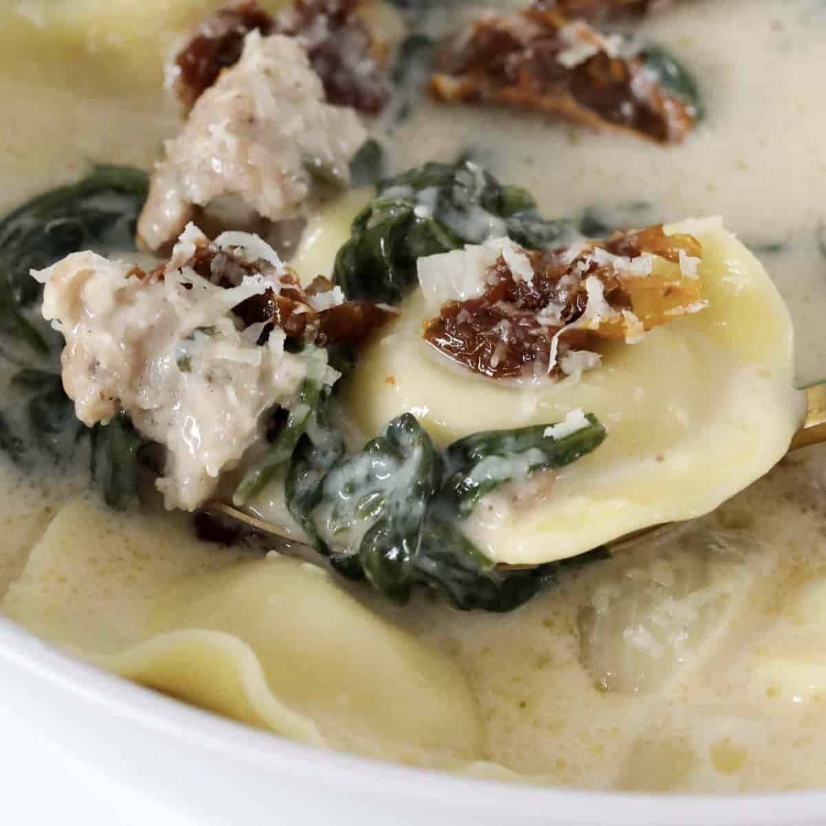 A bowl of creamy soup with sausage, tortellini, spinach and sun-dried tomatoes.