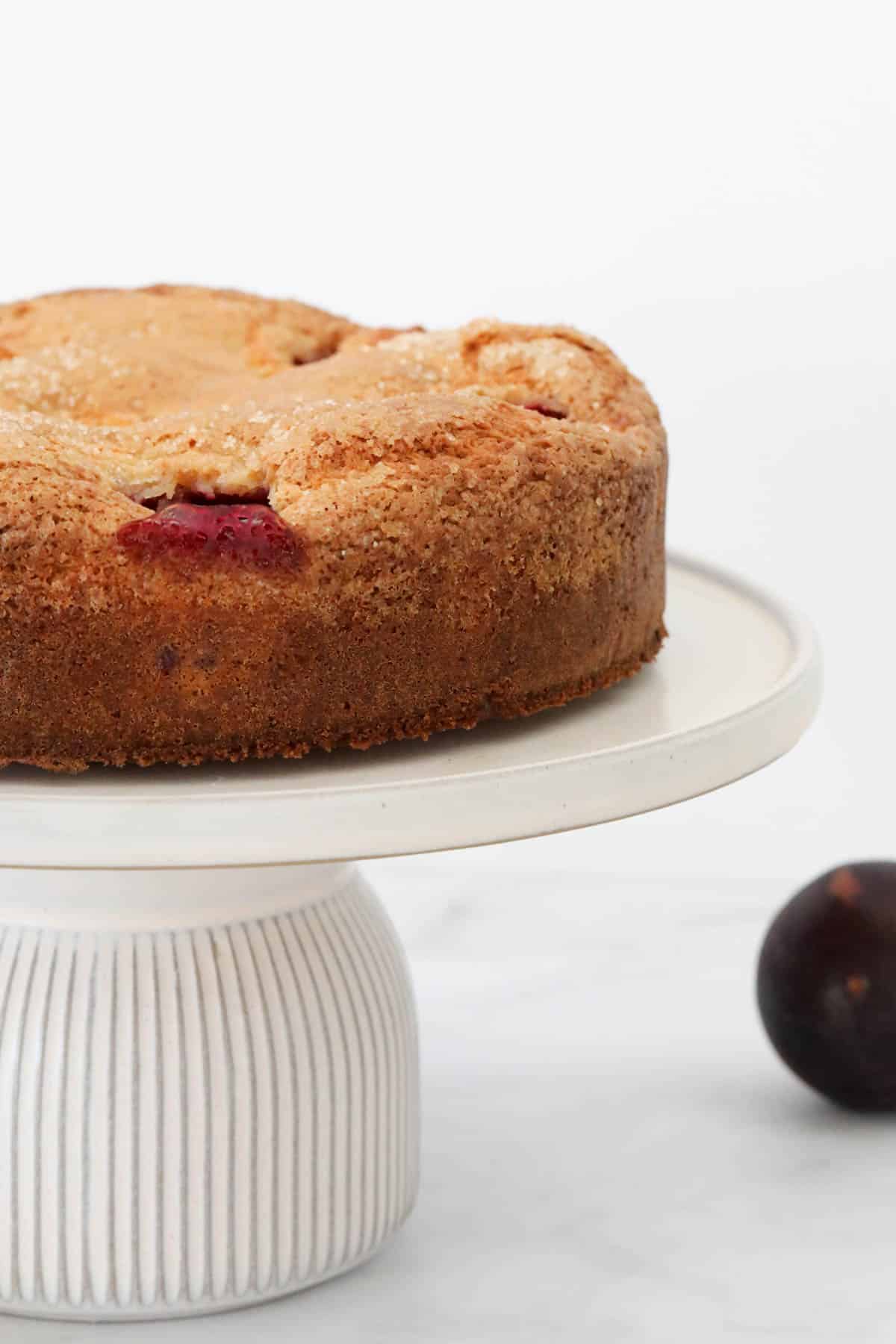 The baked plum cake on a white cake stand.
