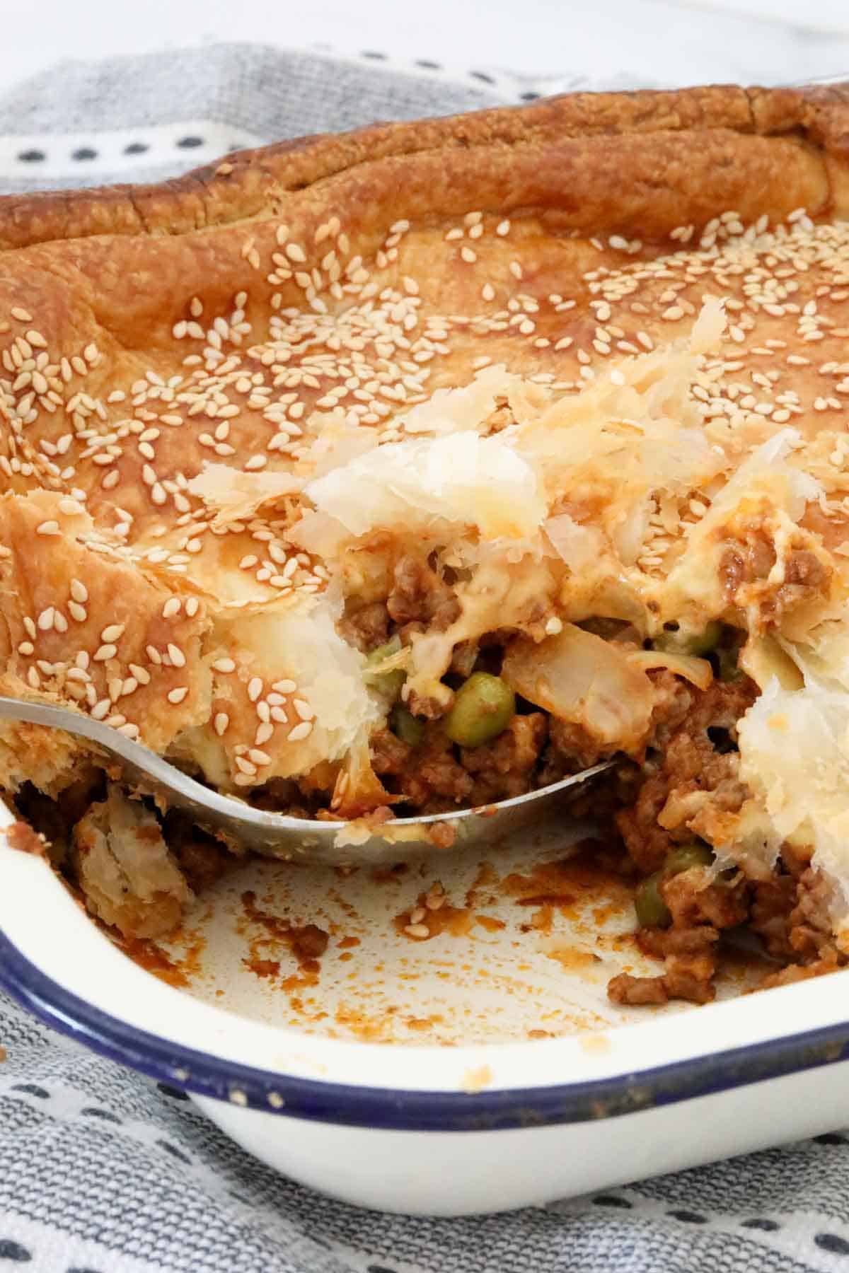 A portion of pie taken out of the baking dish, showing the layers of beef mince and crispy pastry.