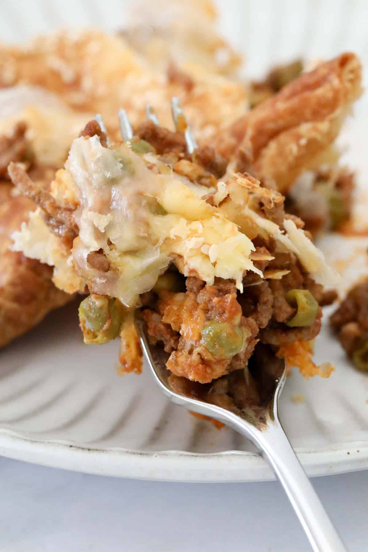 A fork holding up a mouthful of the pie to show the cheese and mince filling.