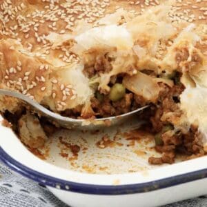 A beef mince filling with peas topped with crispy puff pastry in a pie dish.