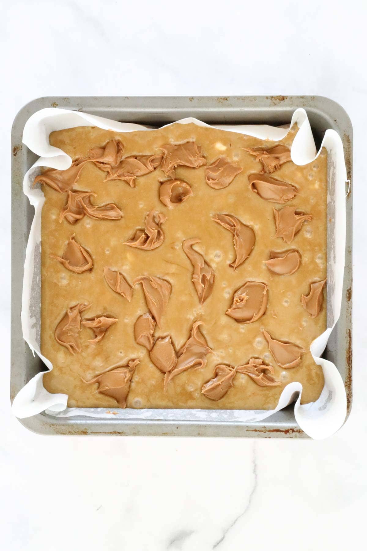 Dollops of Biscoff spread placed over the top of the mixture in the tin.