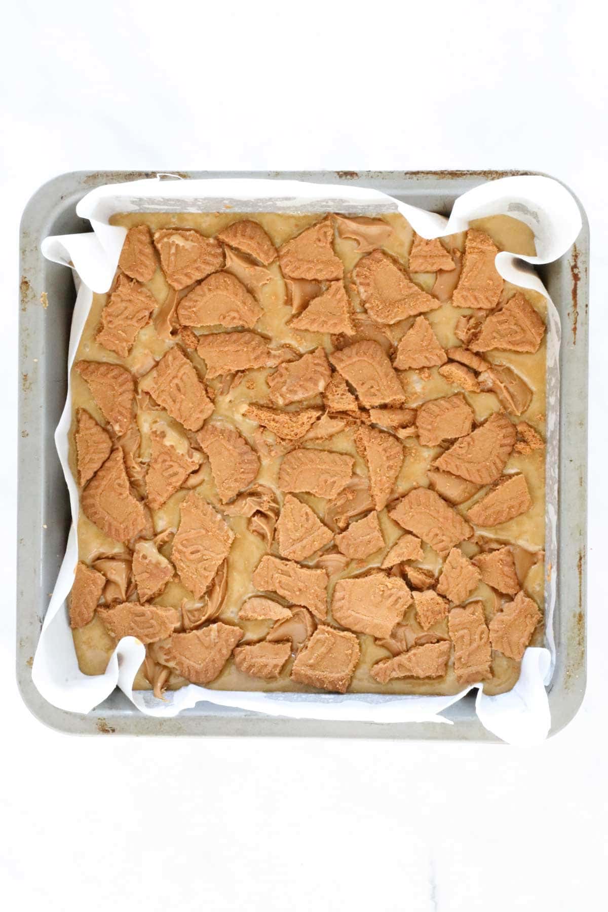 Chunks of Biscoff cookies placed over the mixture in the tin.