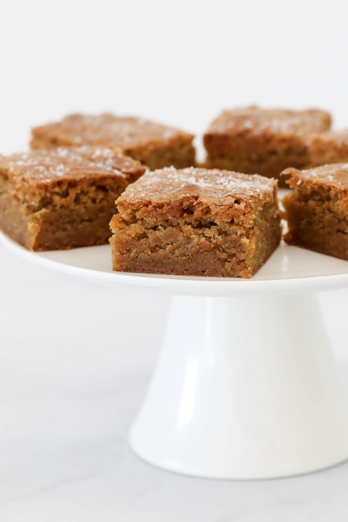 Butterscotch blondies on a white cake stand.