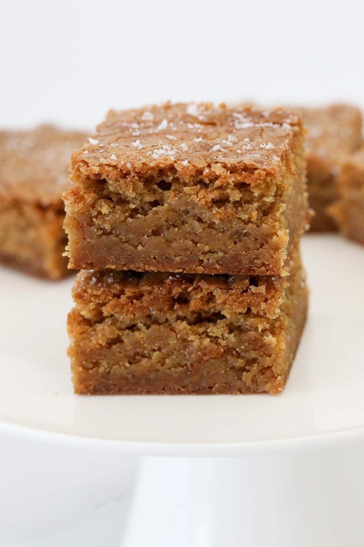 A stack of two butterscotch blondies on a white cake stand.