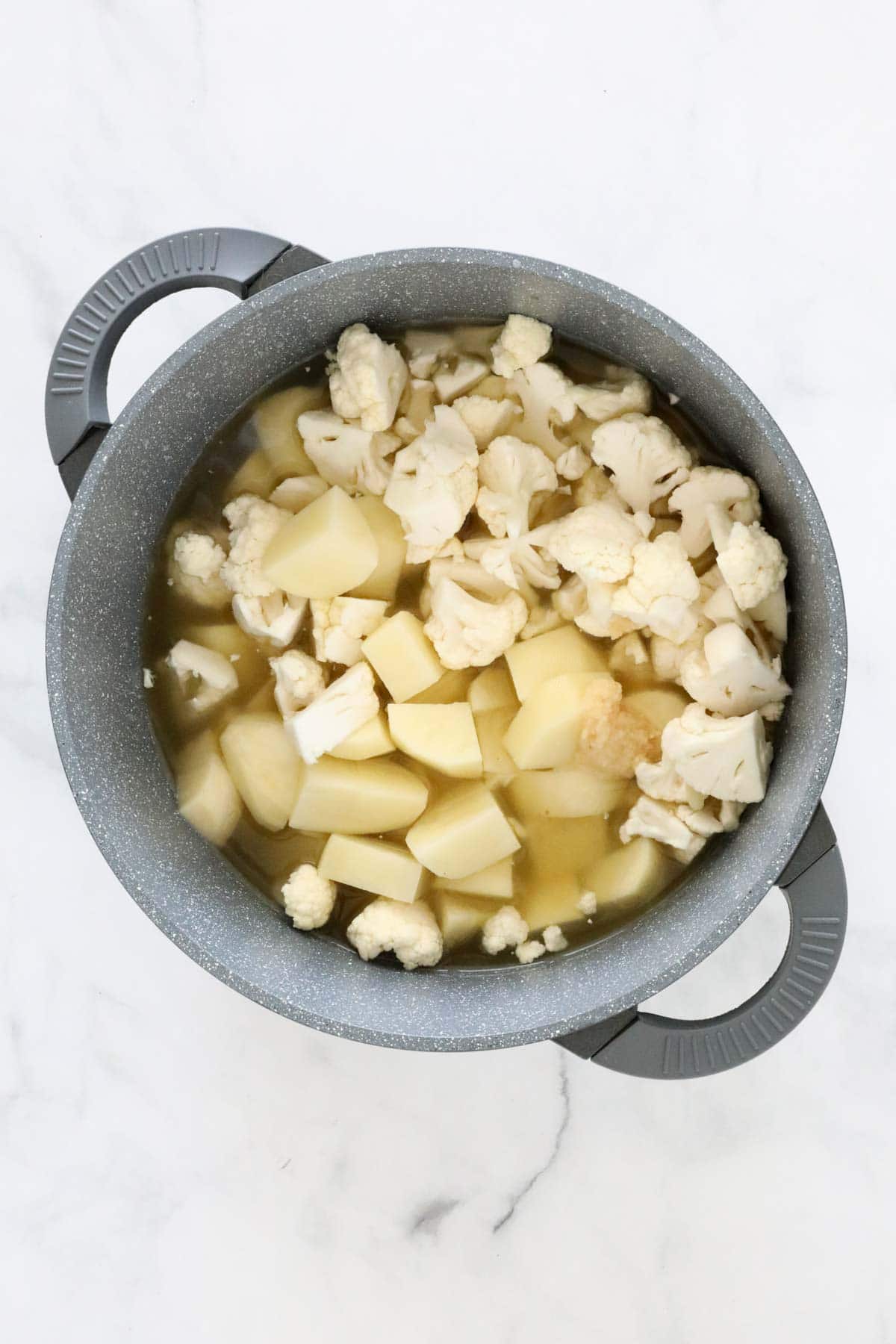 Cubed potatoes, cauli florets and stock in a pot.