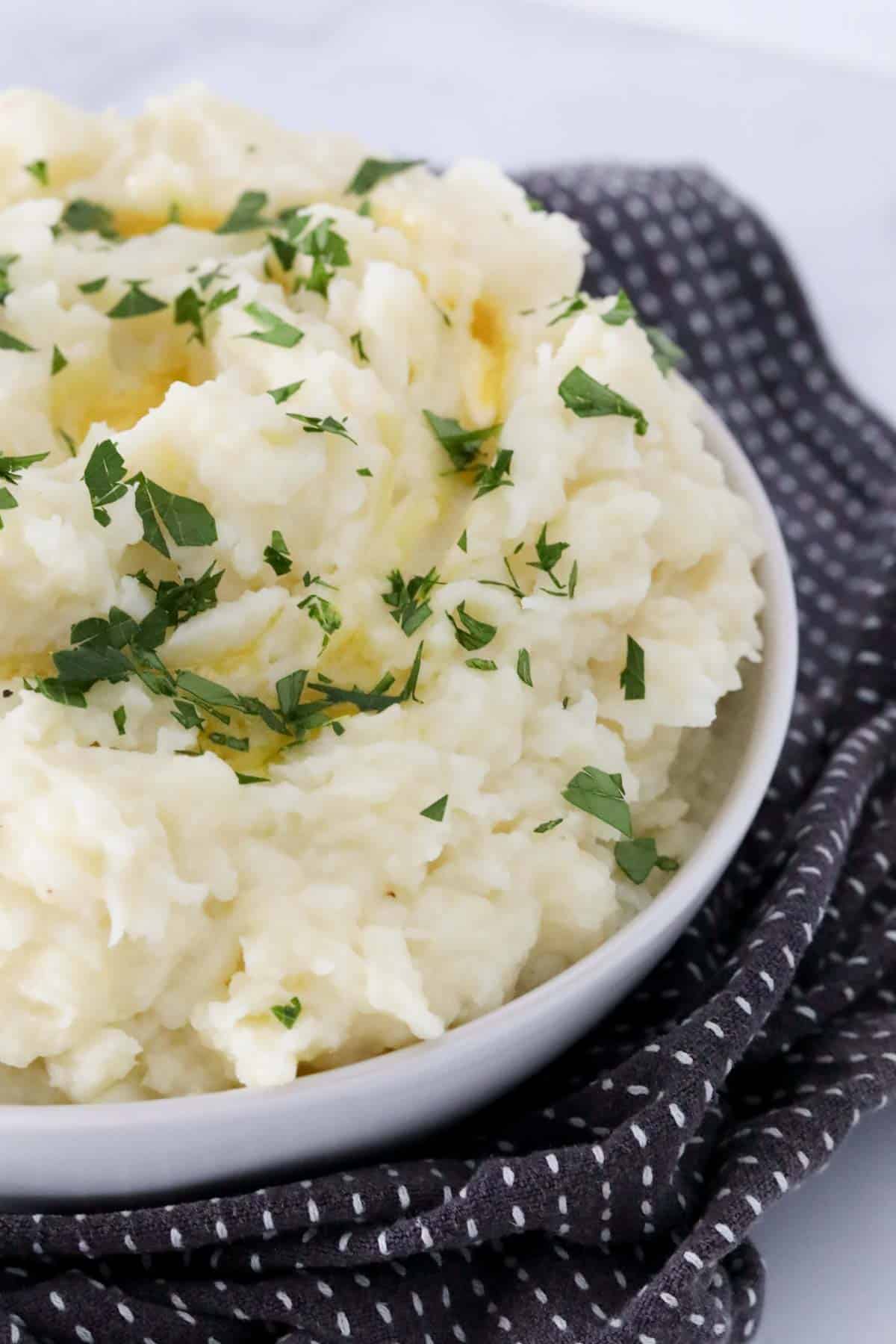 A bowl of mash drizzled with melted butter and sprinkled with fresh parsley.