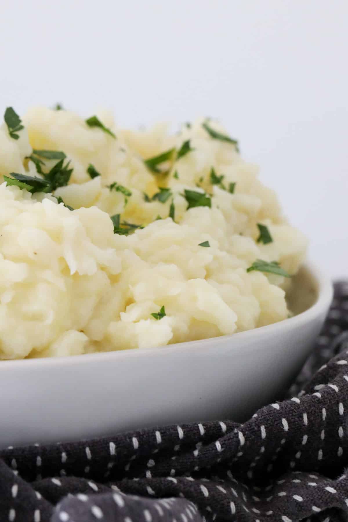 Mashed potatoes and cauliflower in a serving bowl, sprinkled with chopped fresh parsley.