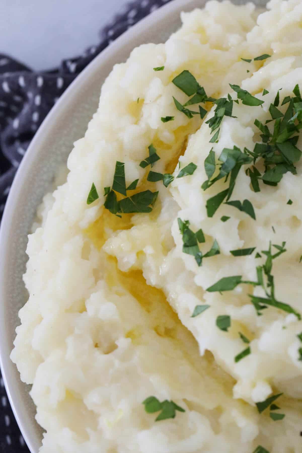 A close up of a bowl of mashed cauliflower and potatoes sprinkled with parsley.