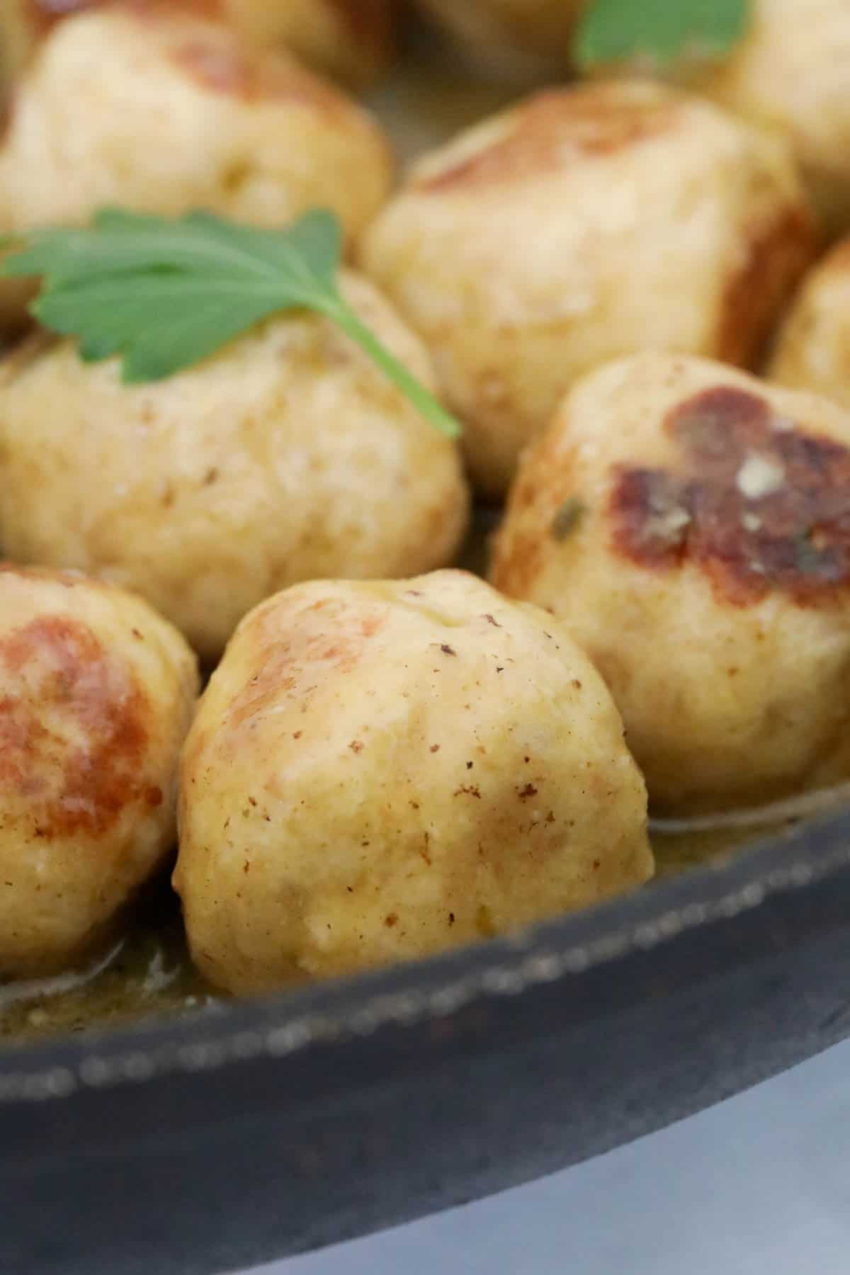 Close up of the cooked chicken meatballs with caper butter sauce in the frying pan.