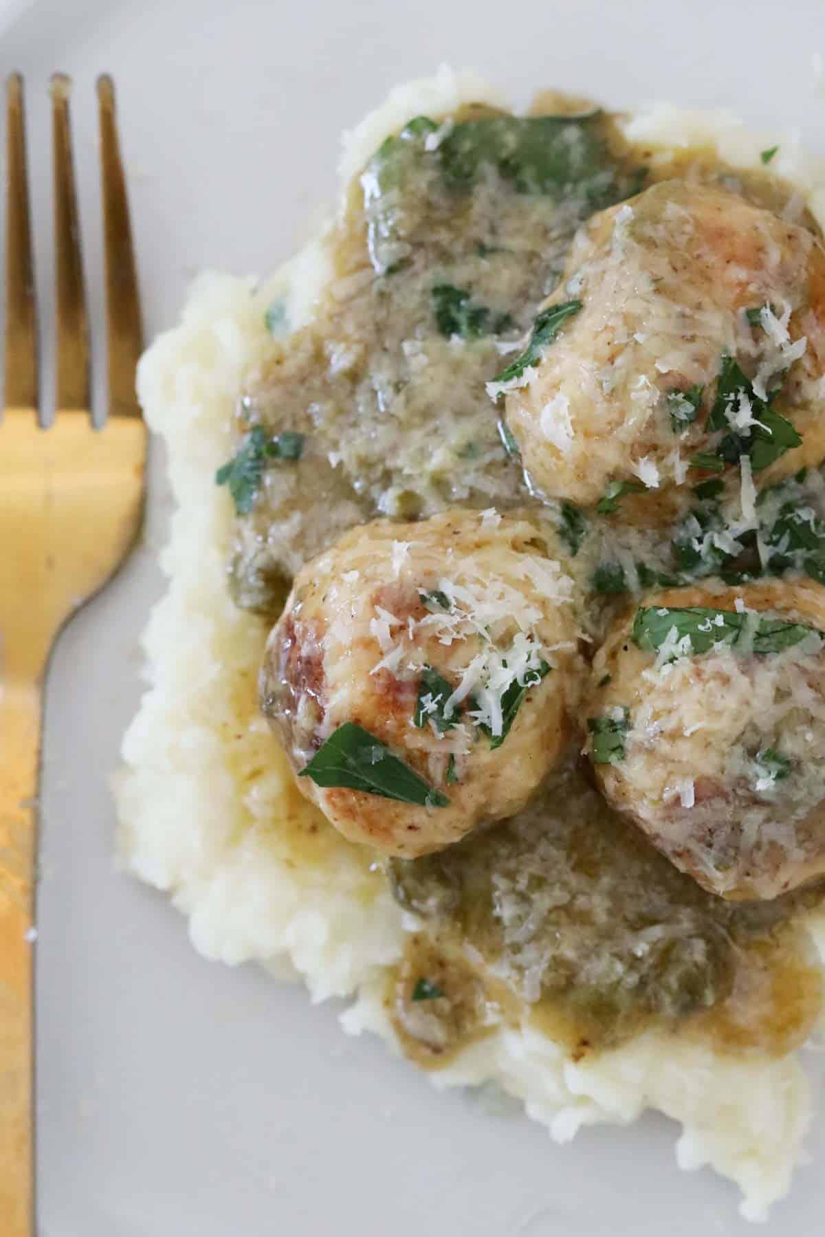 A serving of chicken piccata meatballs on top of mashed potato.