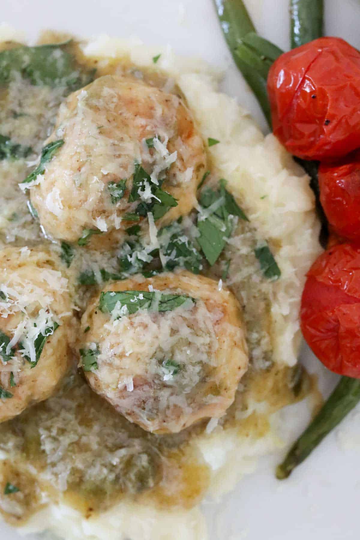 Chicken piccata meatballs on a white plate served with vegetables.