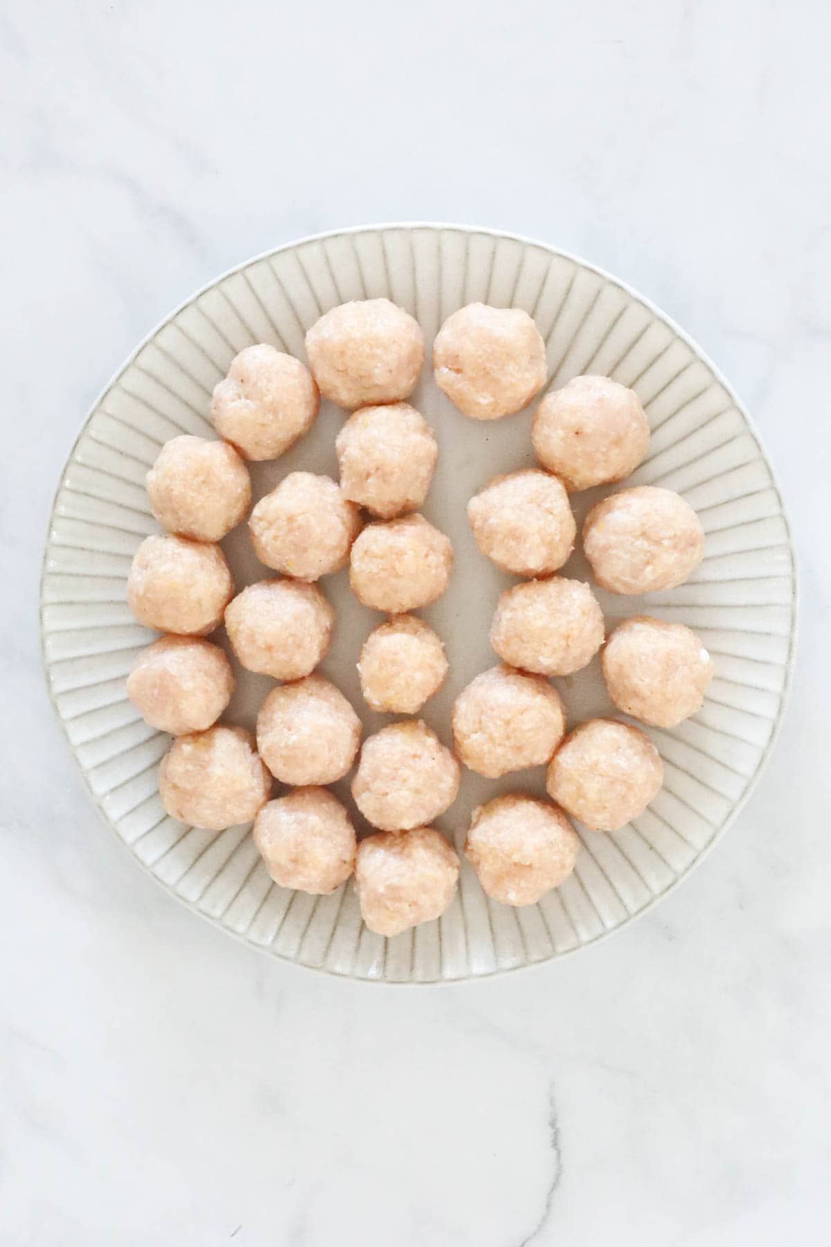 The chicken meatball mixture rolled into meatballs and placed on a plate.