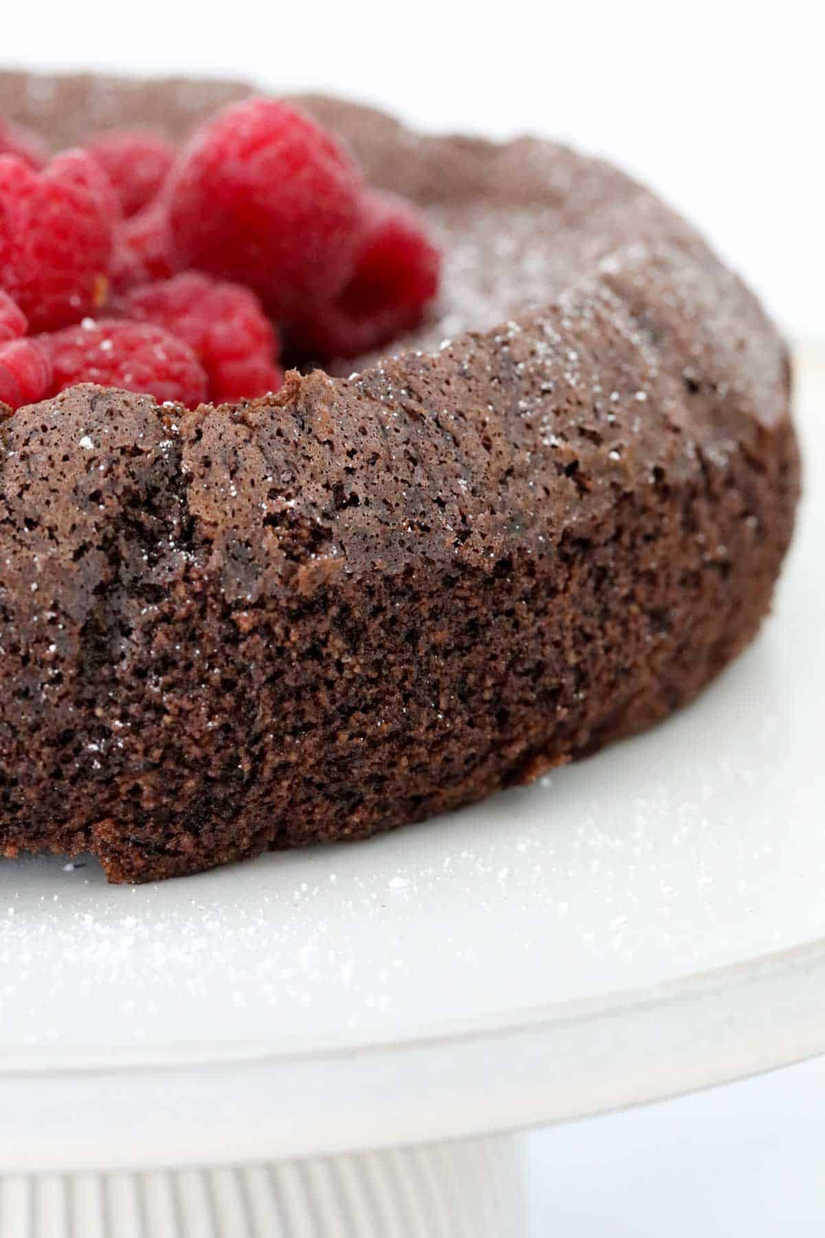 Side view of a dense chocolate cake with fresh raspberries on top.