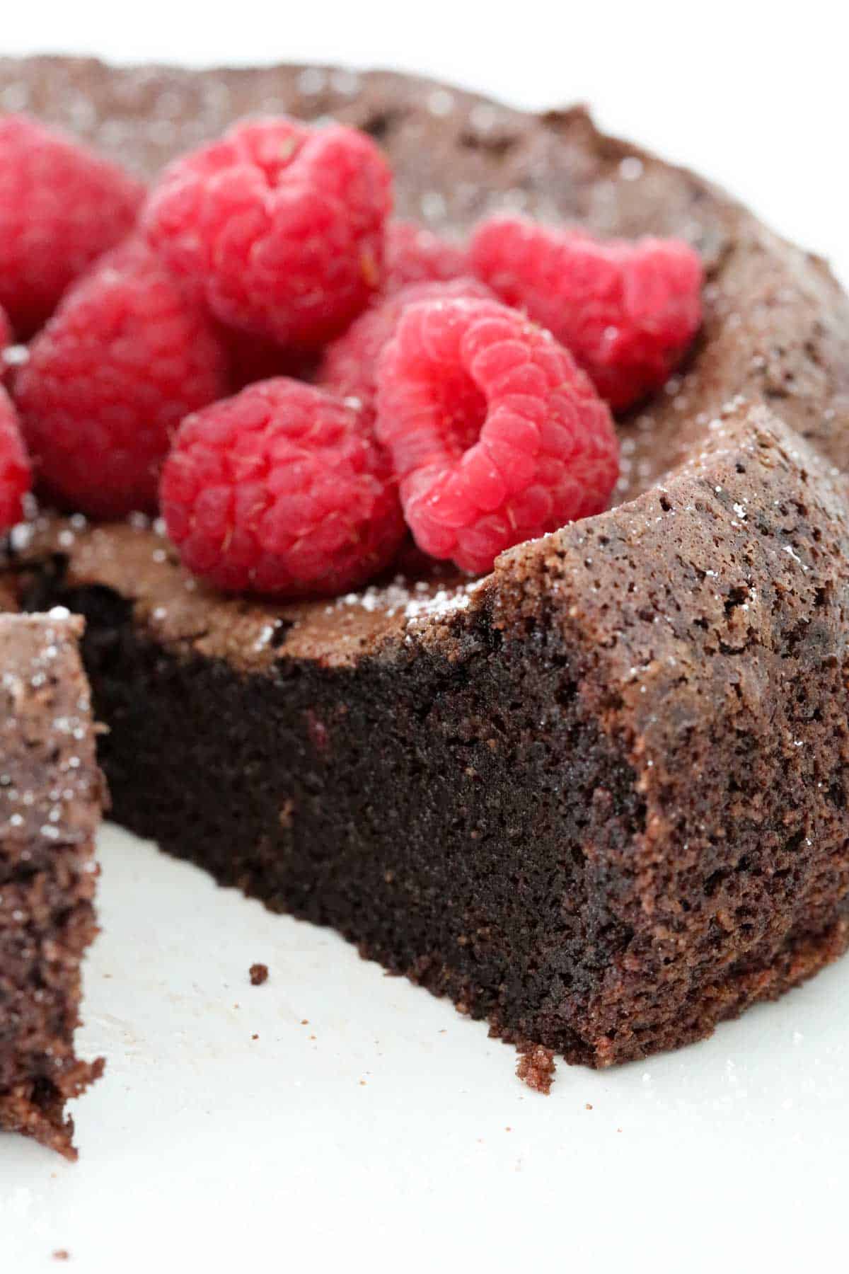 Chocolate cake served with fresh raspberries, with one slice removed.