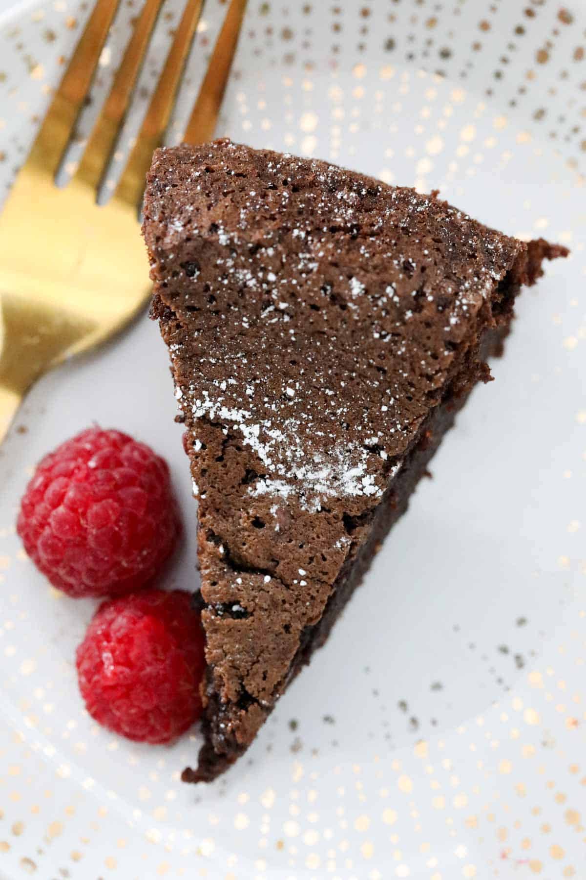 An overhead shot of a wedge of olive oil chocolate cake with fresh raspberries on the side.