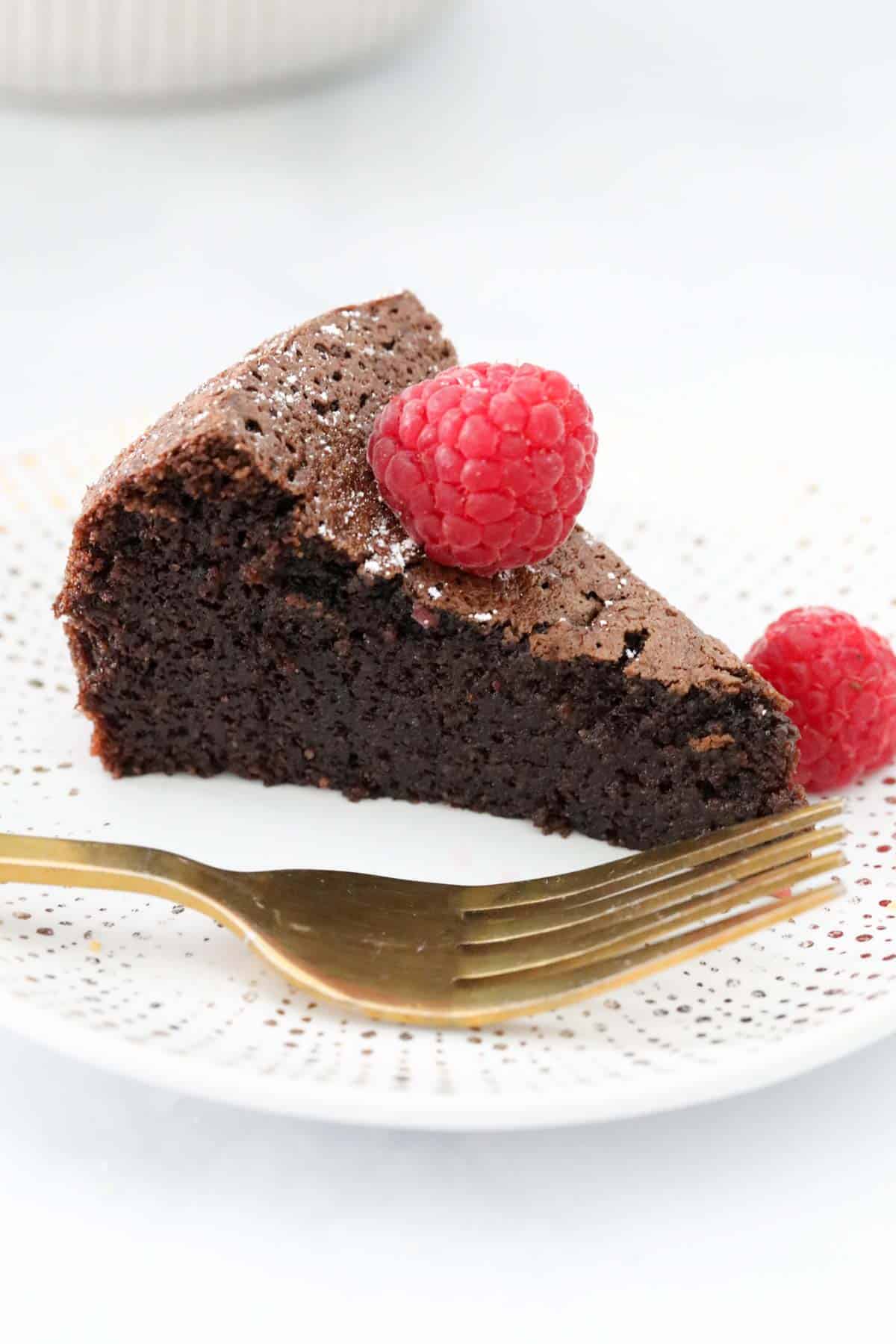 A gold fork resting on a plate next to a wedge of chocolate olive oil cake.