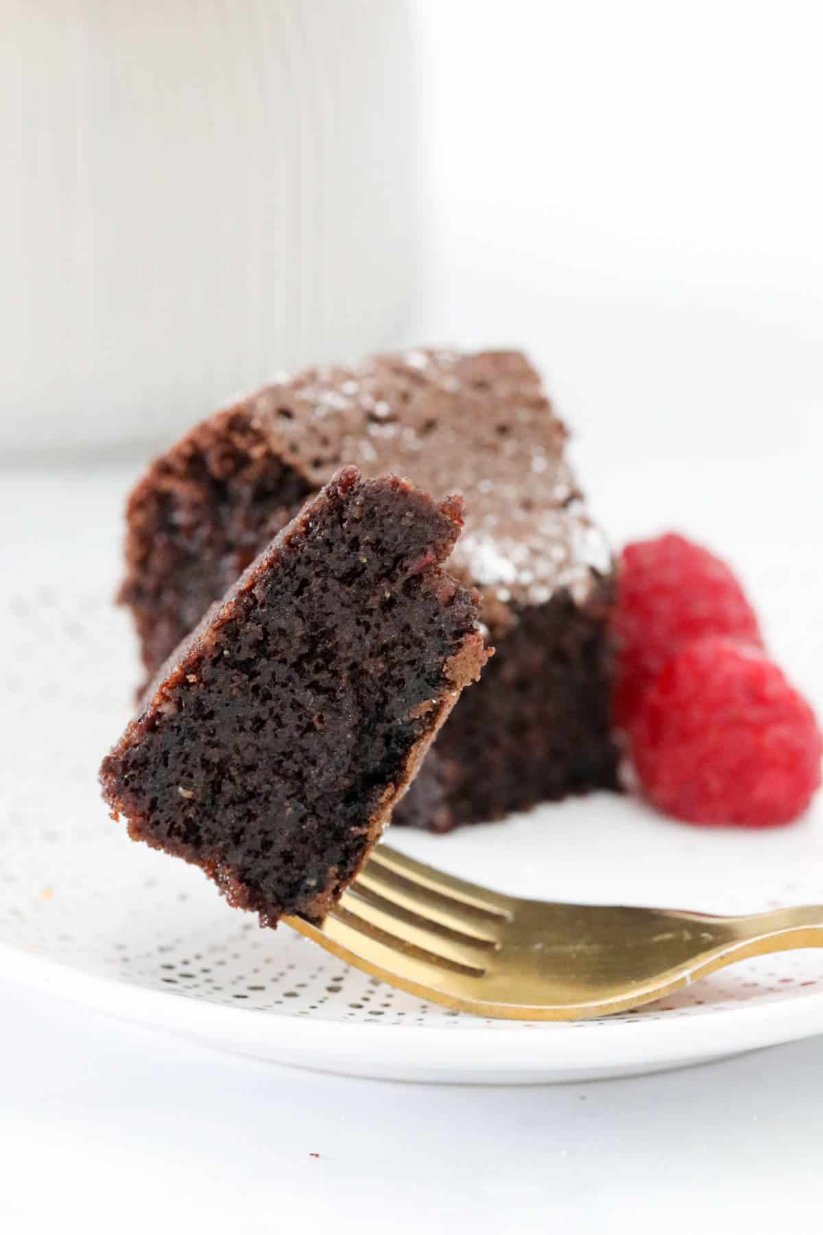 Chocolate cake on a fork, held in front of a serve of cake.