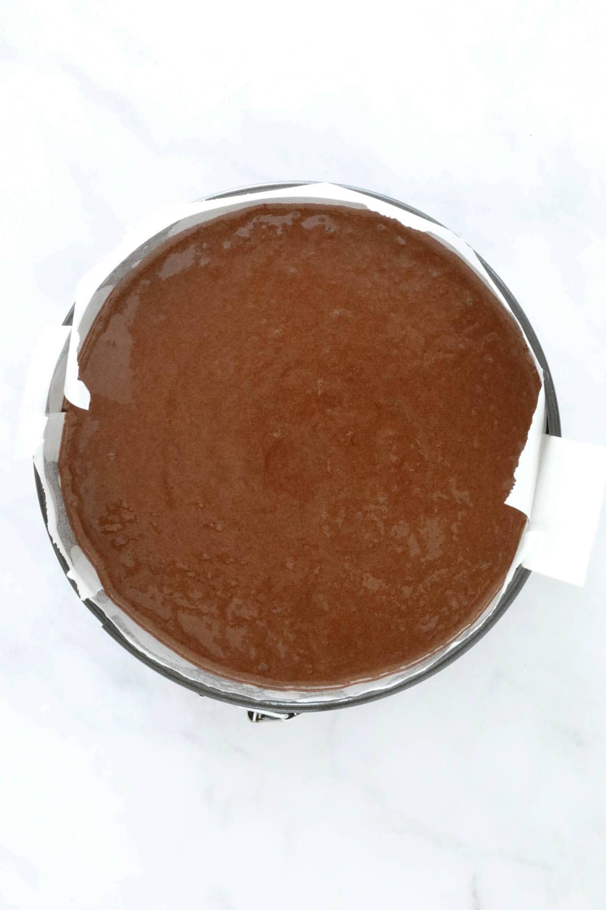 Cake mixture poured into a paper lined round baking tin.