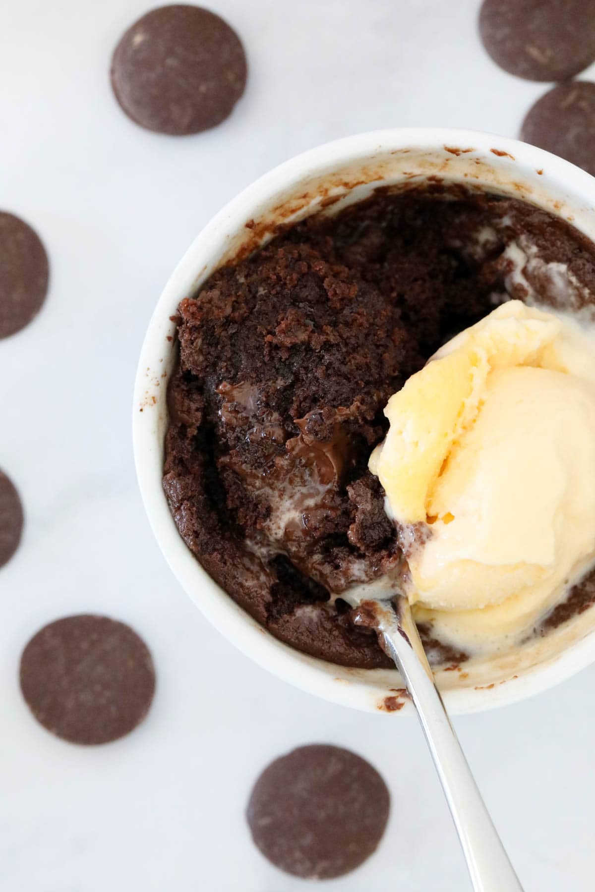 A spoon in a rich chocolate mug cake with ice cream.