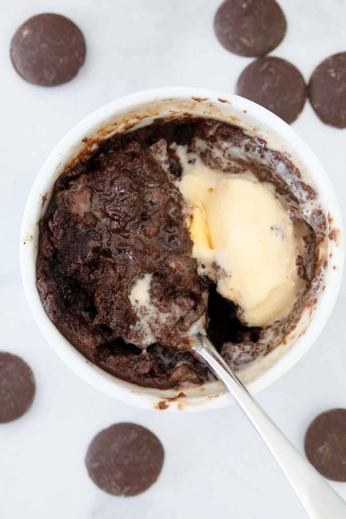 Chocolate mug cake with ice cream melting on top, and a spoon holding up some of the liquid centre.