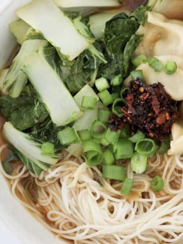 A bowl of noodle soup with dumplings, bok choy, spring onions and chilli.