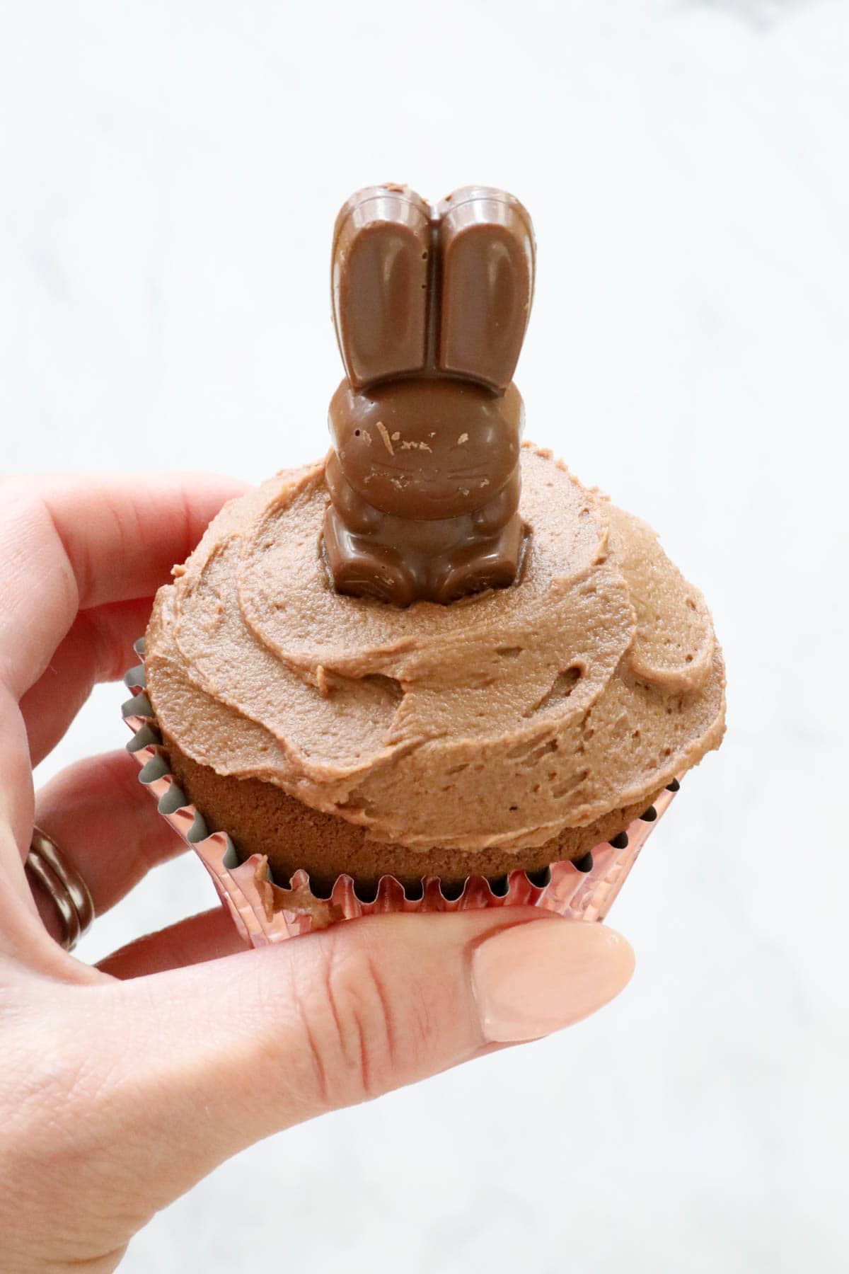 A hand holding an Easter cupcake with a chocolate bunny on top.