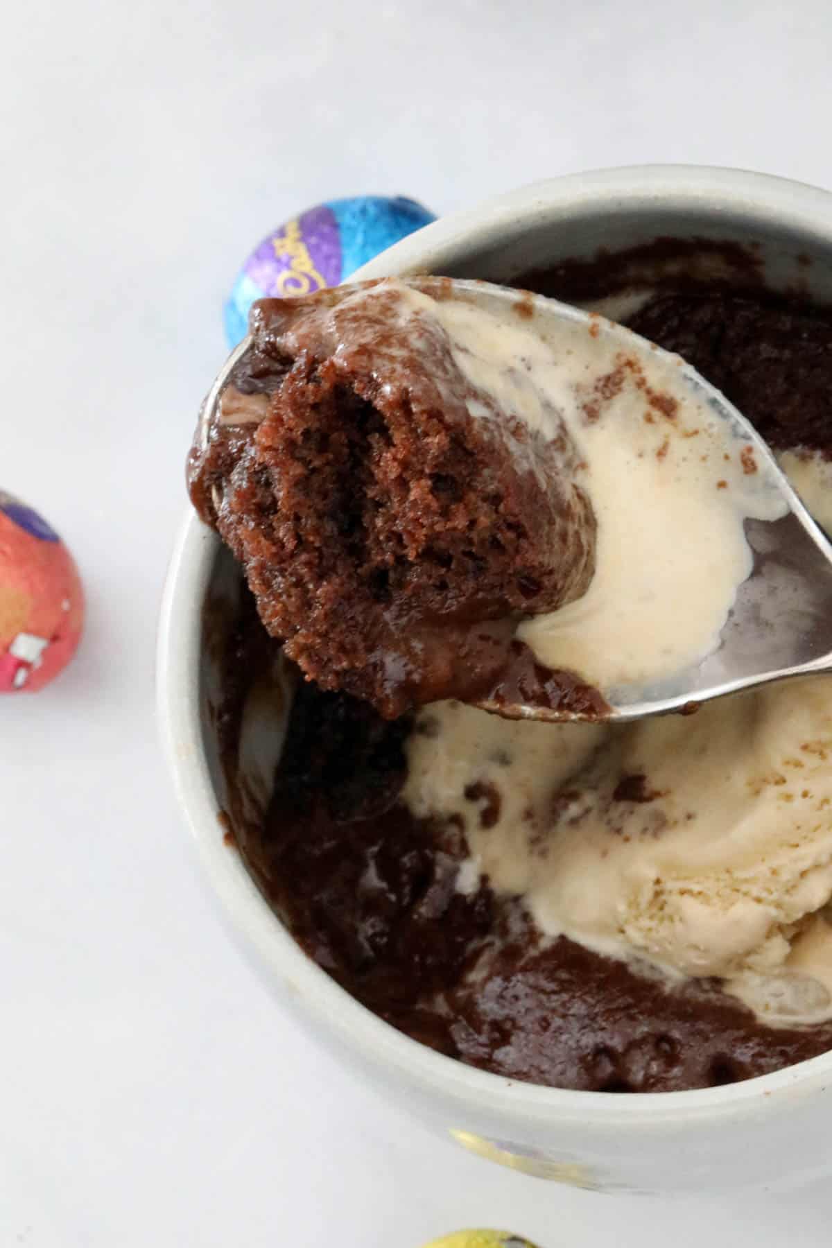 A spoon holding up a portion of the chocolate cake with some ice cream.