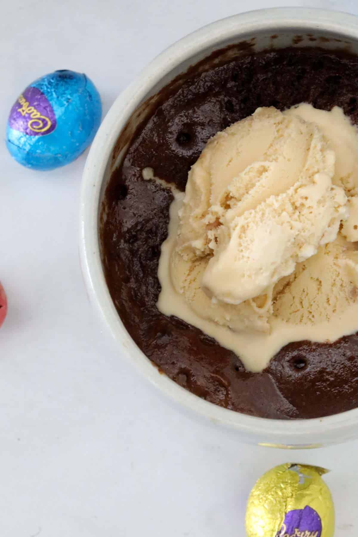 Easter egg mug cake topped with a scoop of ice cream, and mini eggs scattered around the mug.