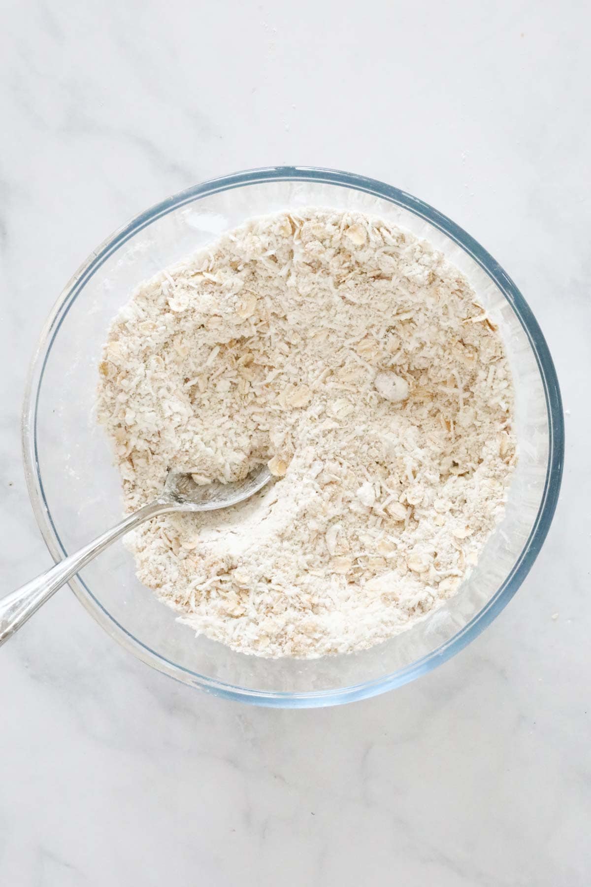 Oats, gluten free flour and coconut mixed in a mixing bowl.
